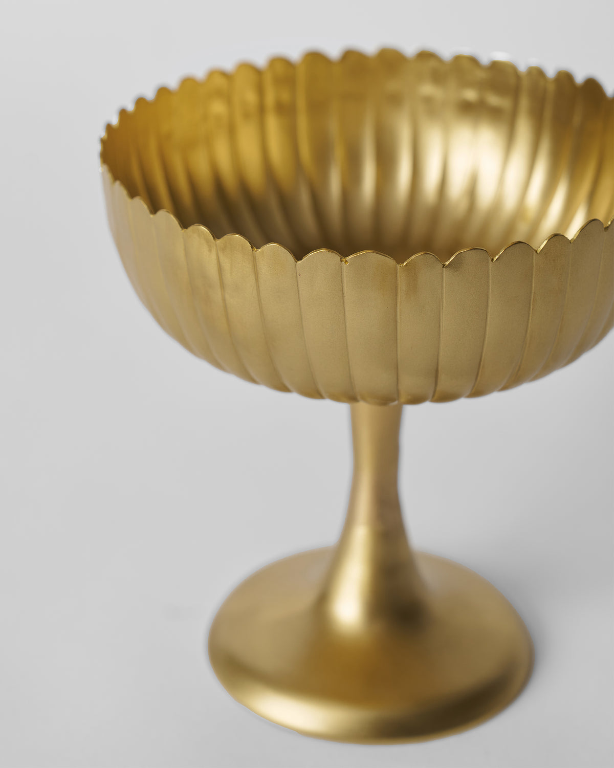 Three-quarter view into a fluted gold Dhaara pedestal serving bowl.