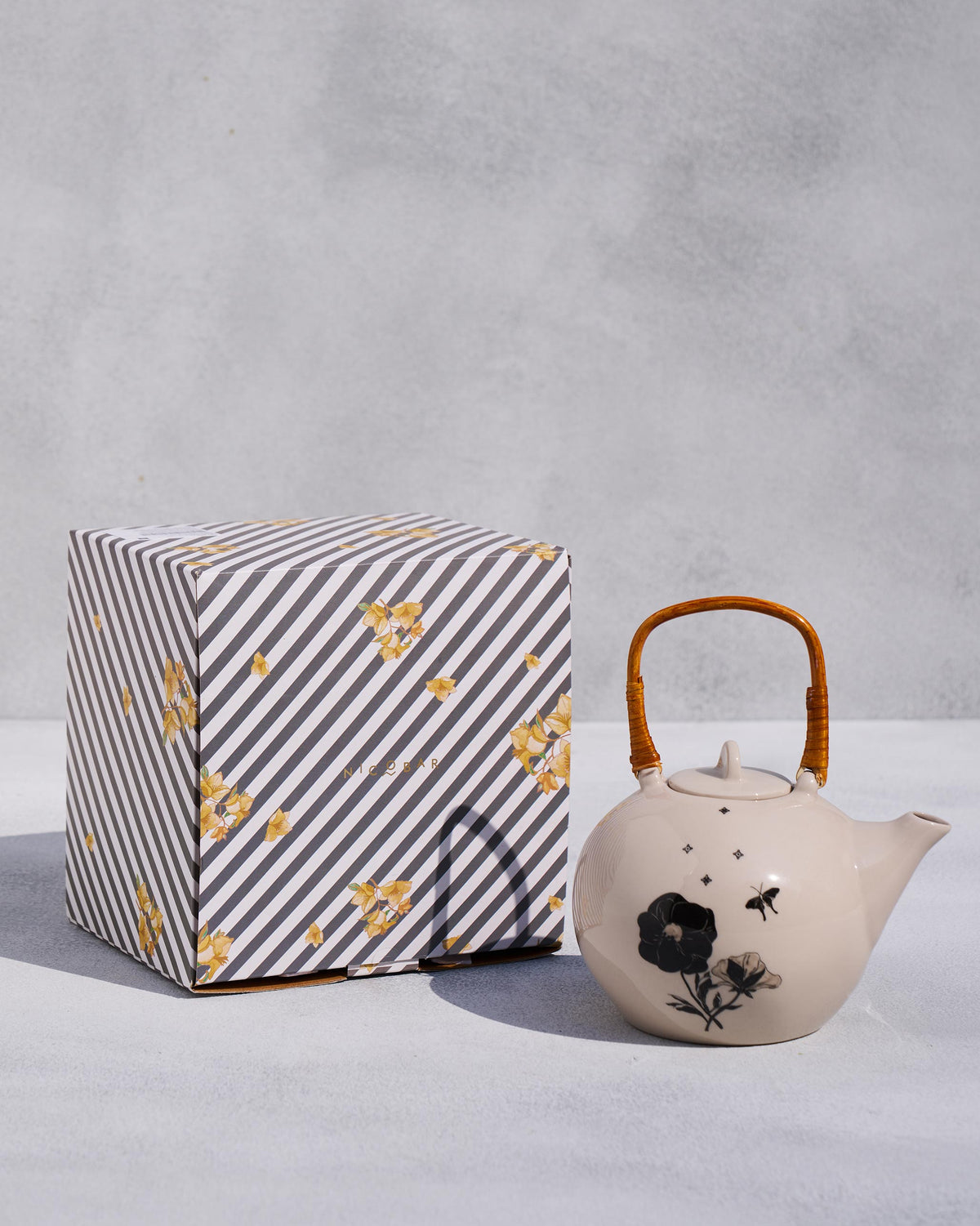 Ivory Poppy teapot with rattan handle beside its striped Nicobar box.