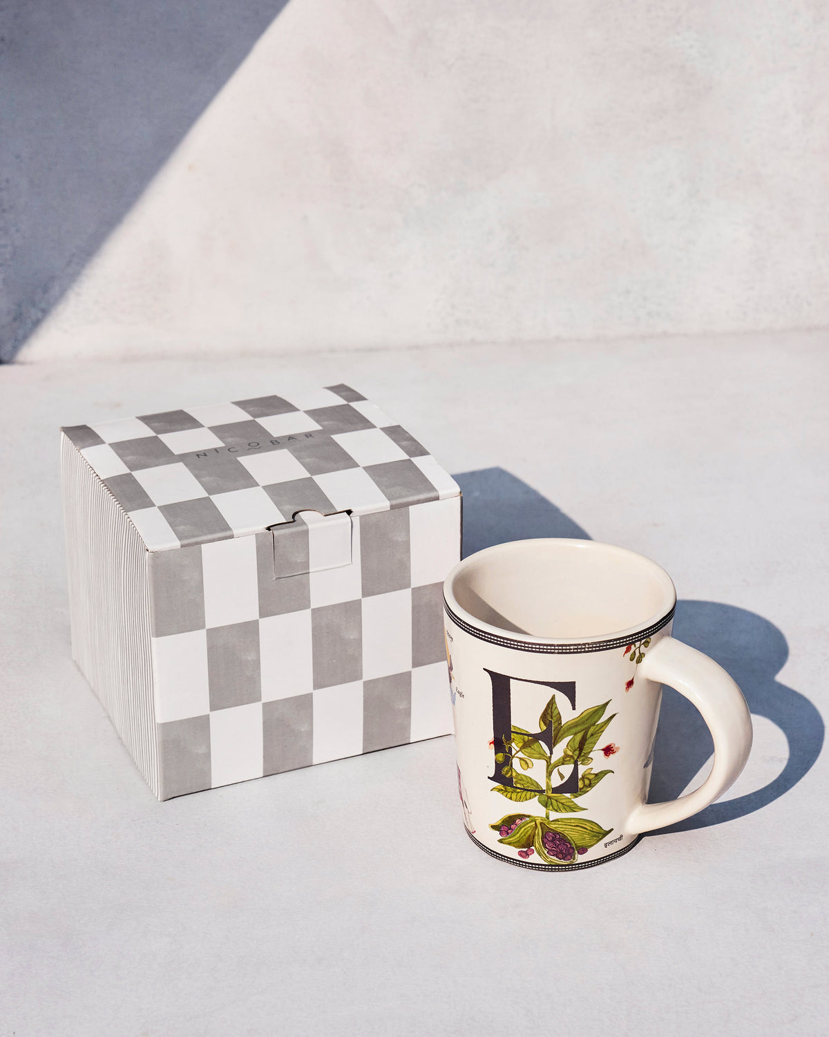 Elaichi mug with a black E and botanicals beside a Nicobar gift box.