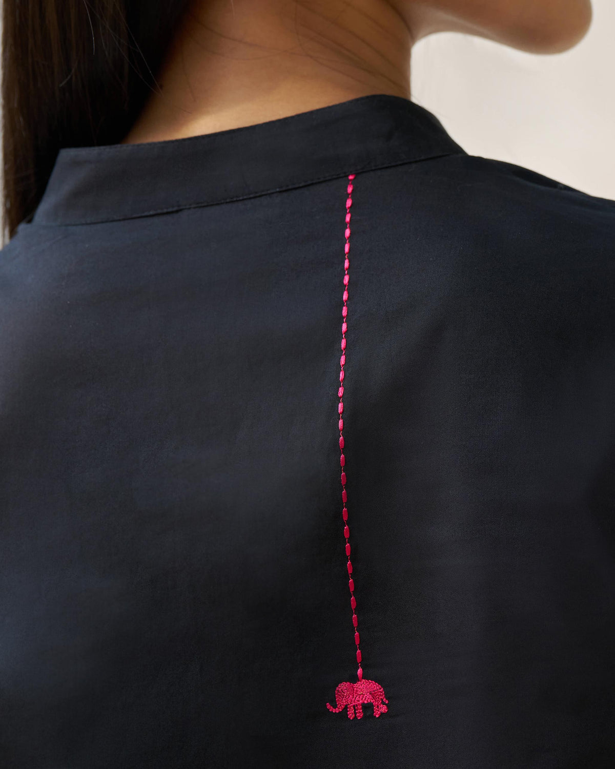 Close-up of a pink elephant embroidery on the back of a black Stone set.