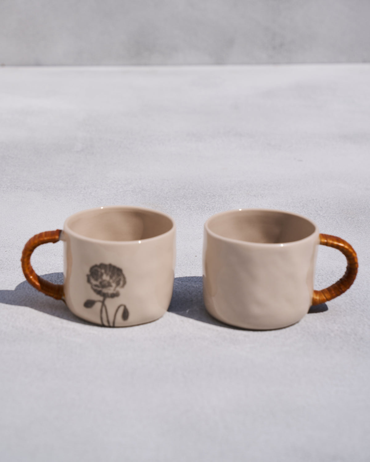 Pair of Poppy mugs with rattan handles and a black poppy print.