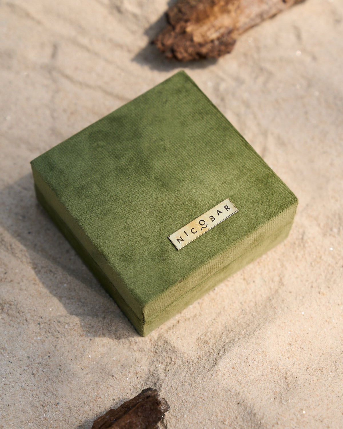 Green velvet Nicobar jewellery box on sand.