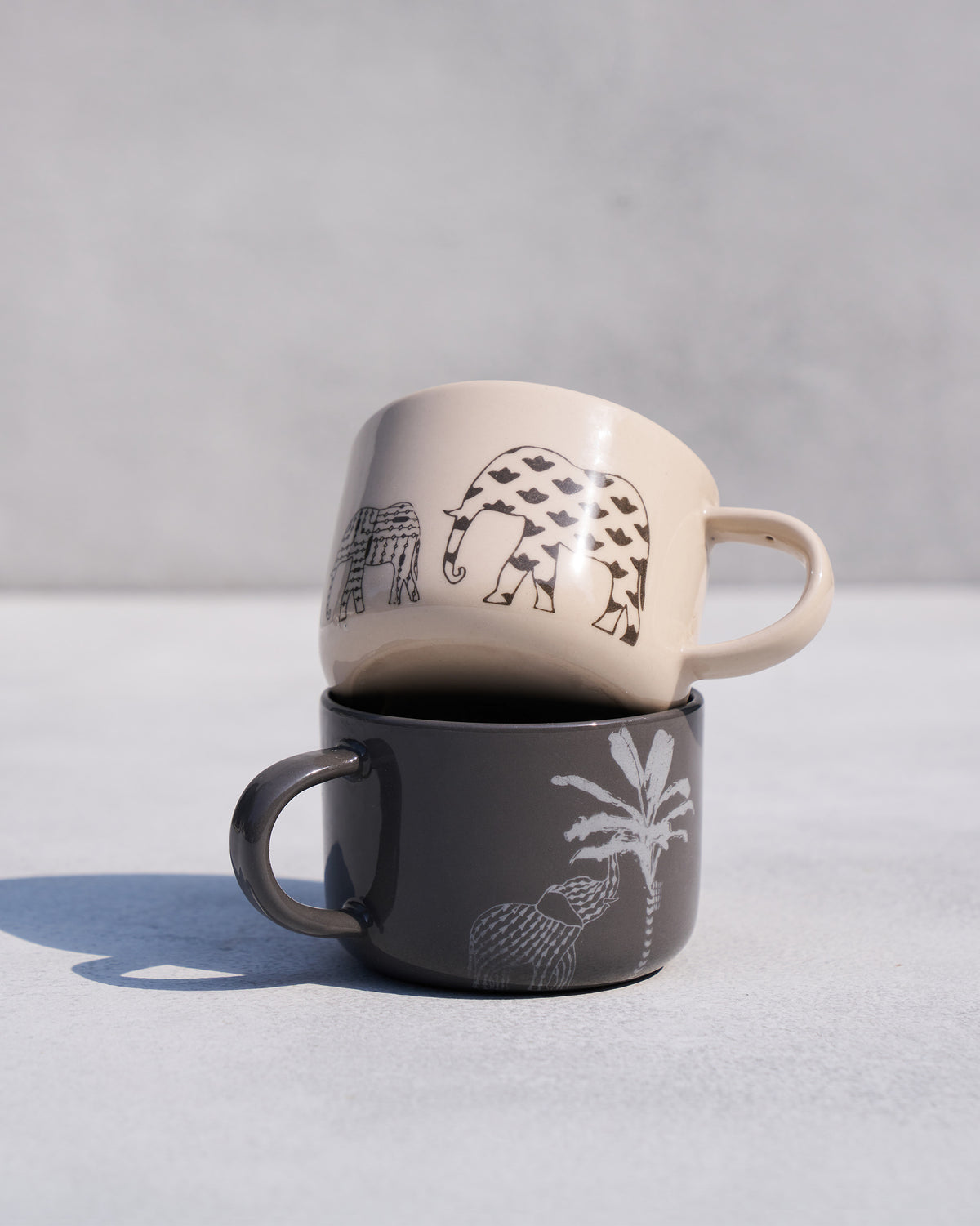 Stacked Coastal Mugs with patterned elephants and a palm tree print.