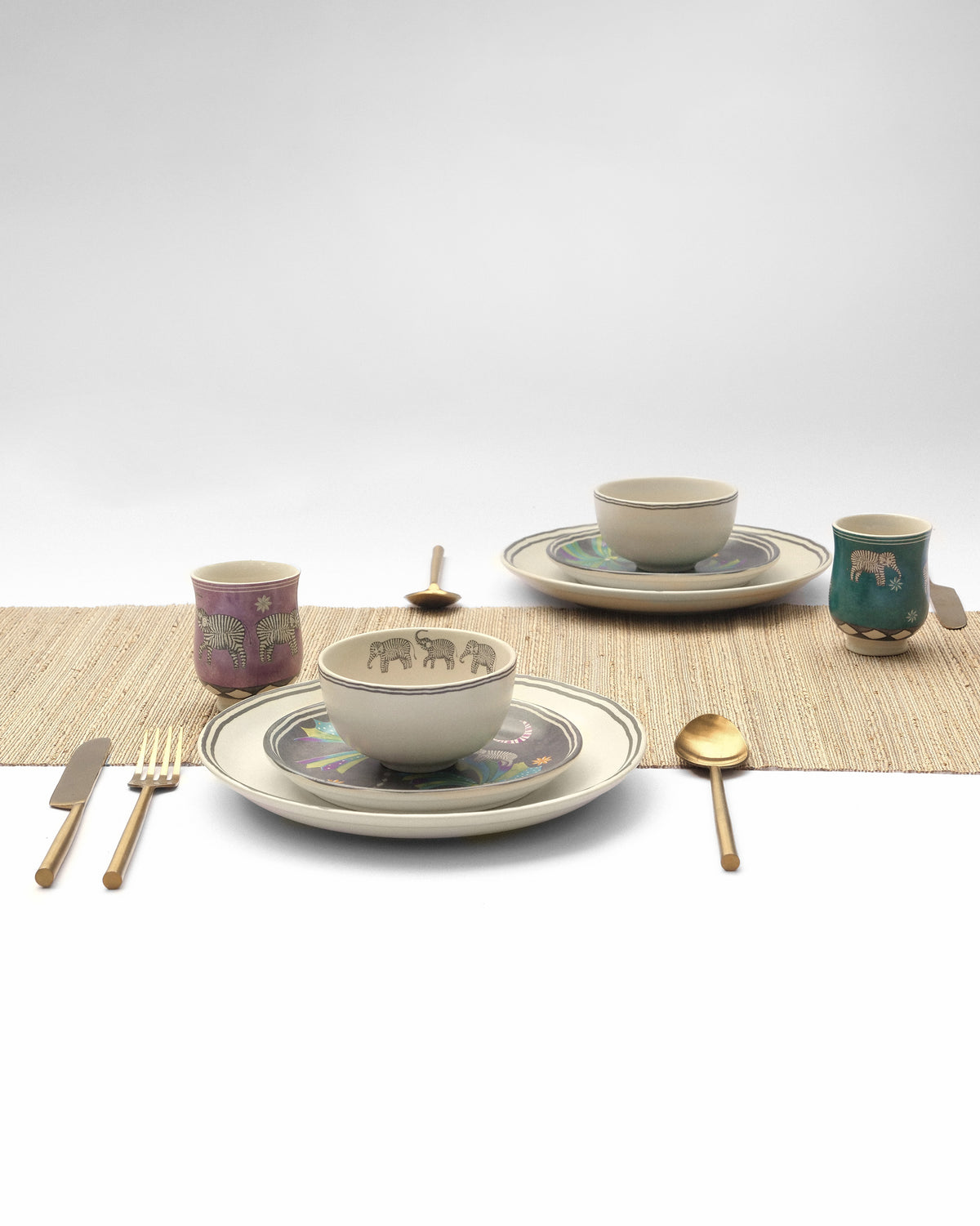 The Tusk Dinner Set for 2 in a table setting with elephant-motif bowls and cups.