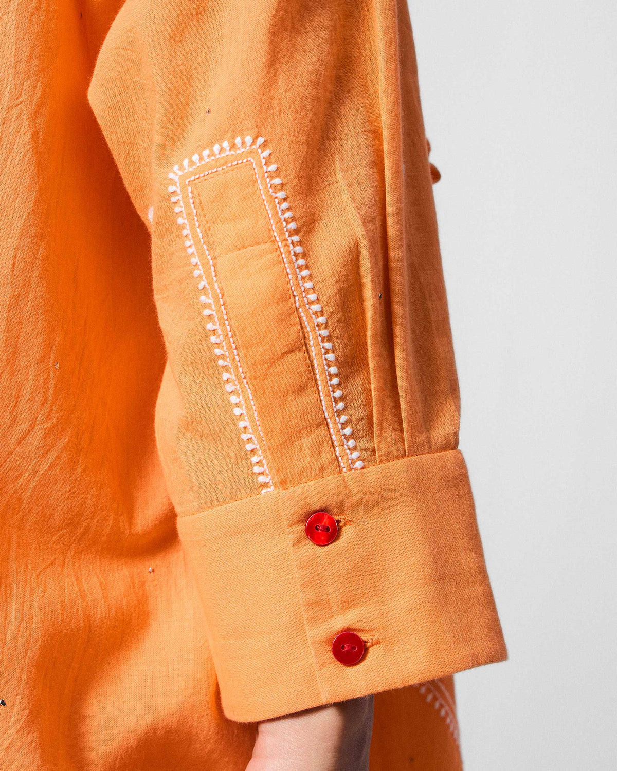 Close-up of white embroidery and red buttons on an orange Lazy Sunday cuff.