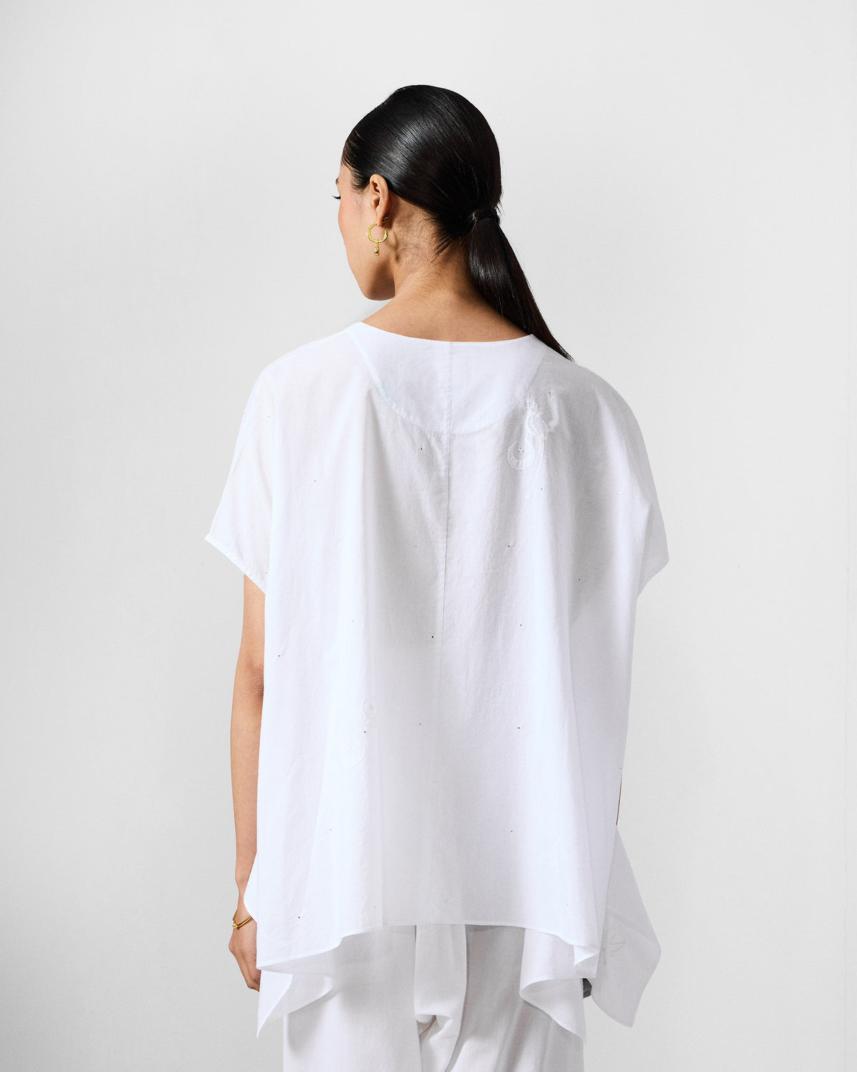 Back of an ivory Riva top with scattered embroidery and a draped hem.