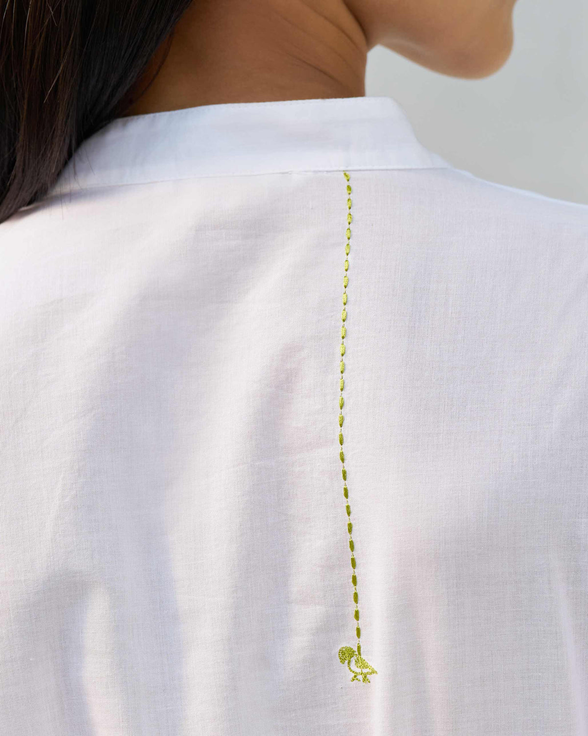 Close-up of a green embroidered bird on the back of a white kurta.