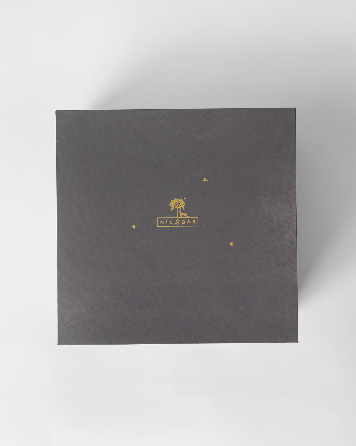 Charcoal Nicobar gift box lid with a gold palm tree logo.