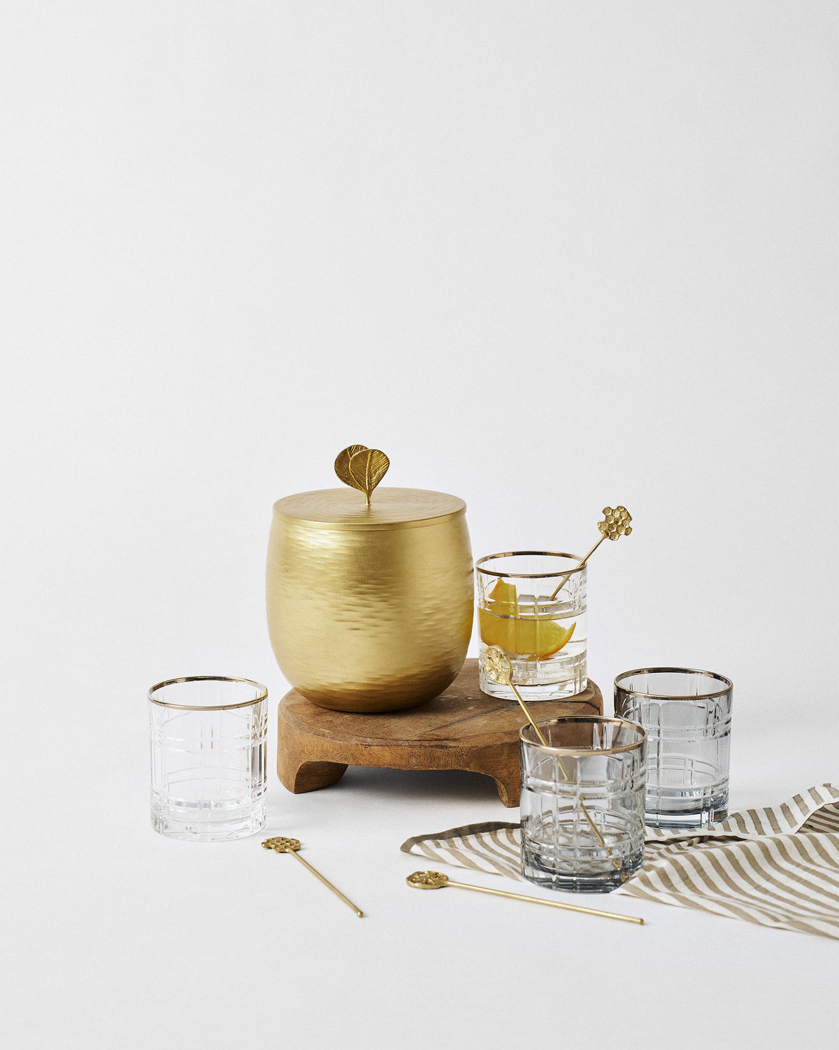 The Celeste glasses, gold ice bucket and stirrers set out on a wooden stand.