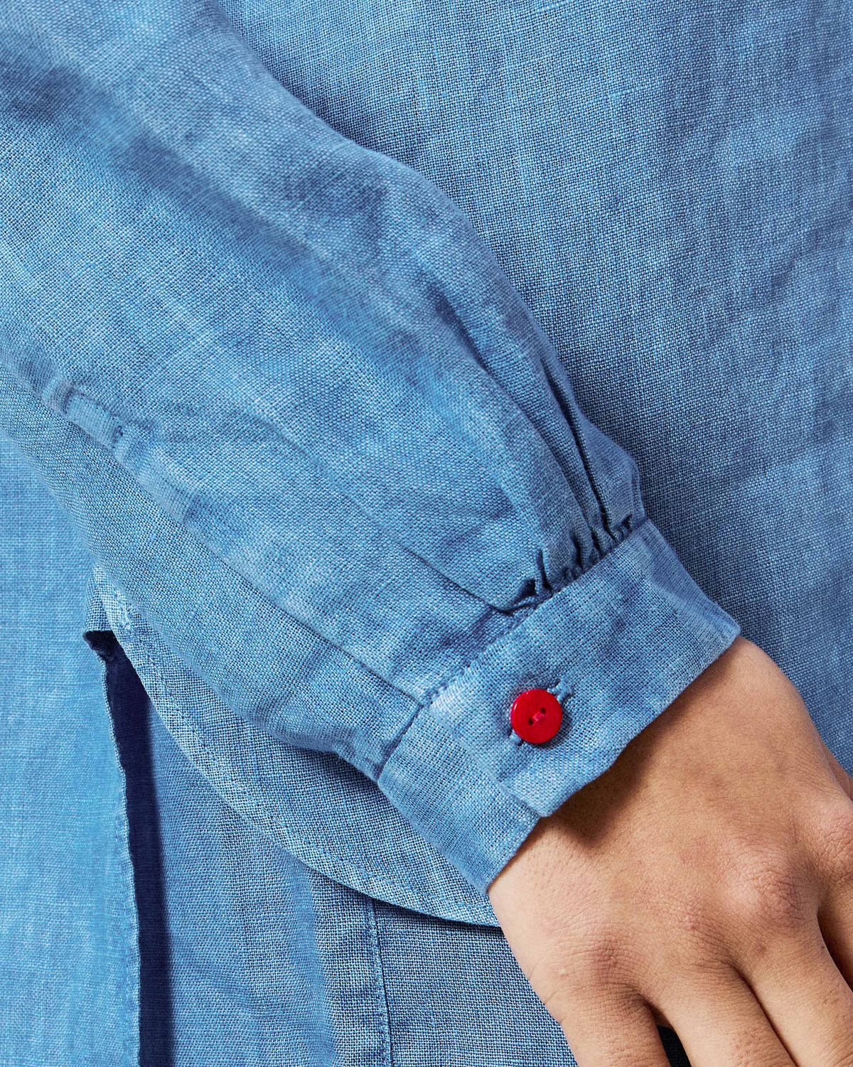 Close-up of a blue Mati shirt showing a red button on the cuff.