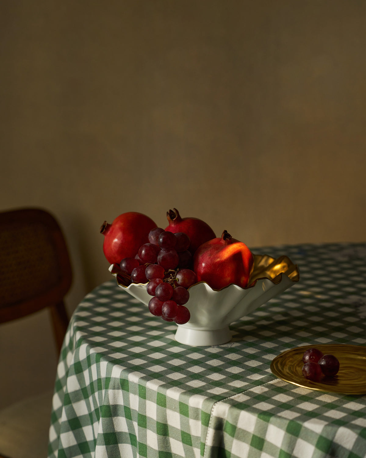 Dhaara Fruit Bowl holding pomegranates and grapes on a green checked tablecloth.