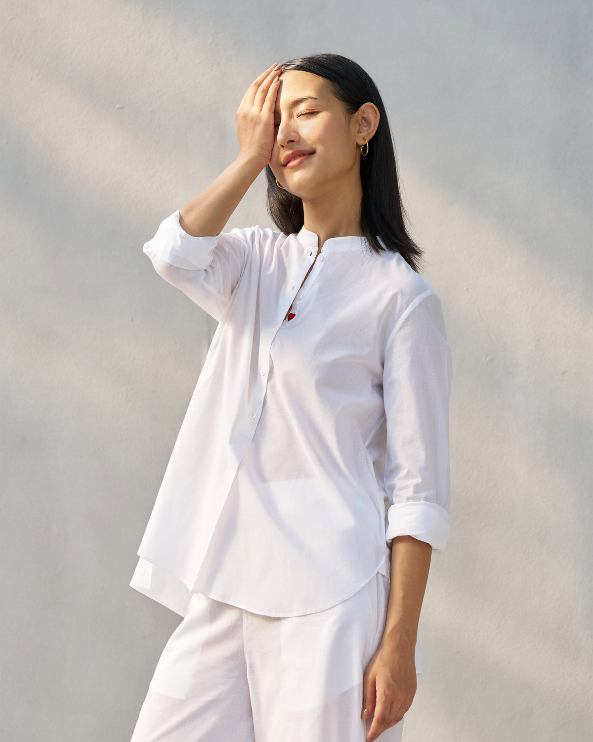 Person wearing a white mandarin collar top with a red heart on the placket.