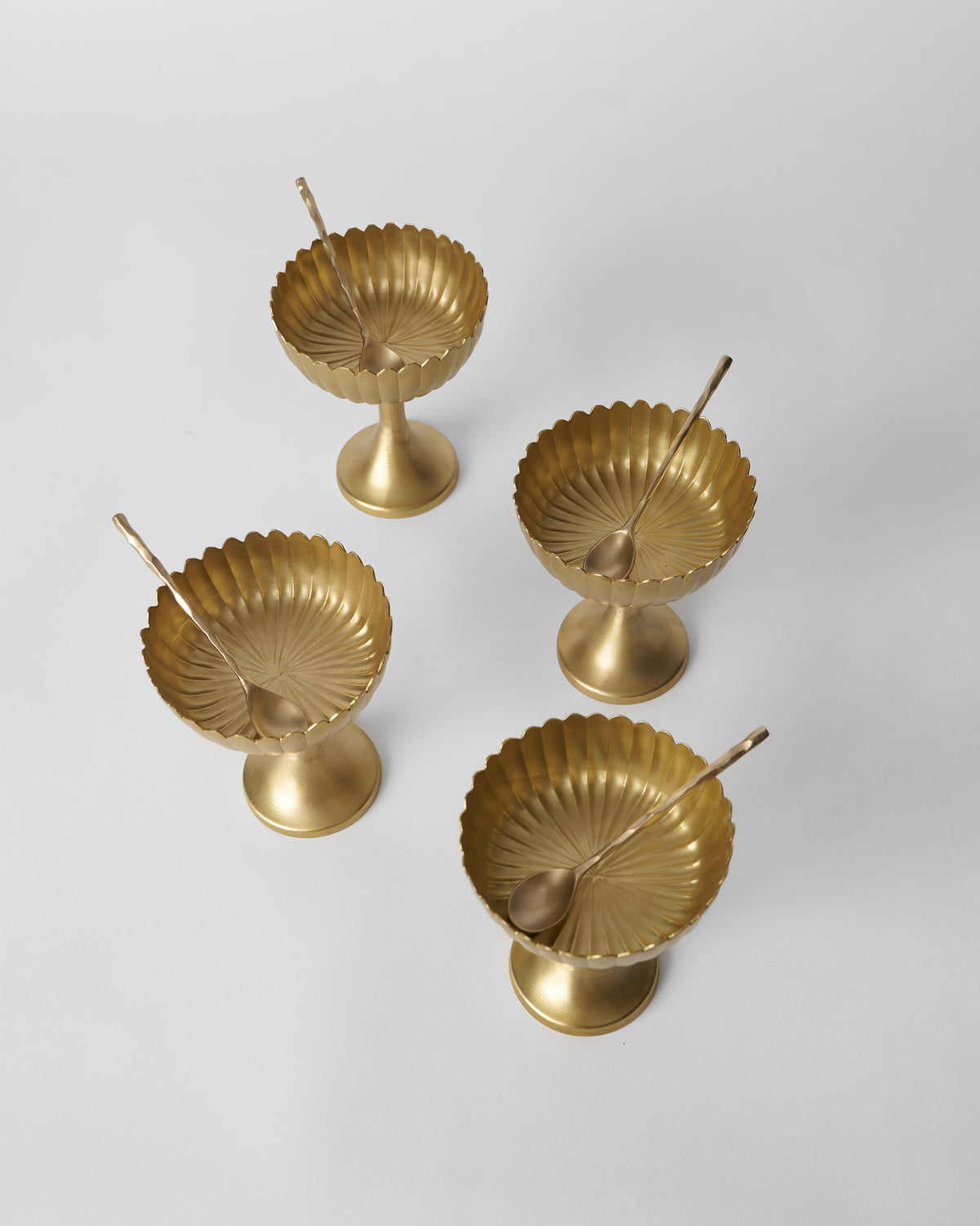 Overhead view of four gold Dhaara Gelato Cups with spoons inside.