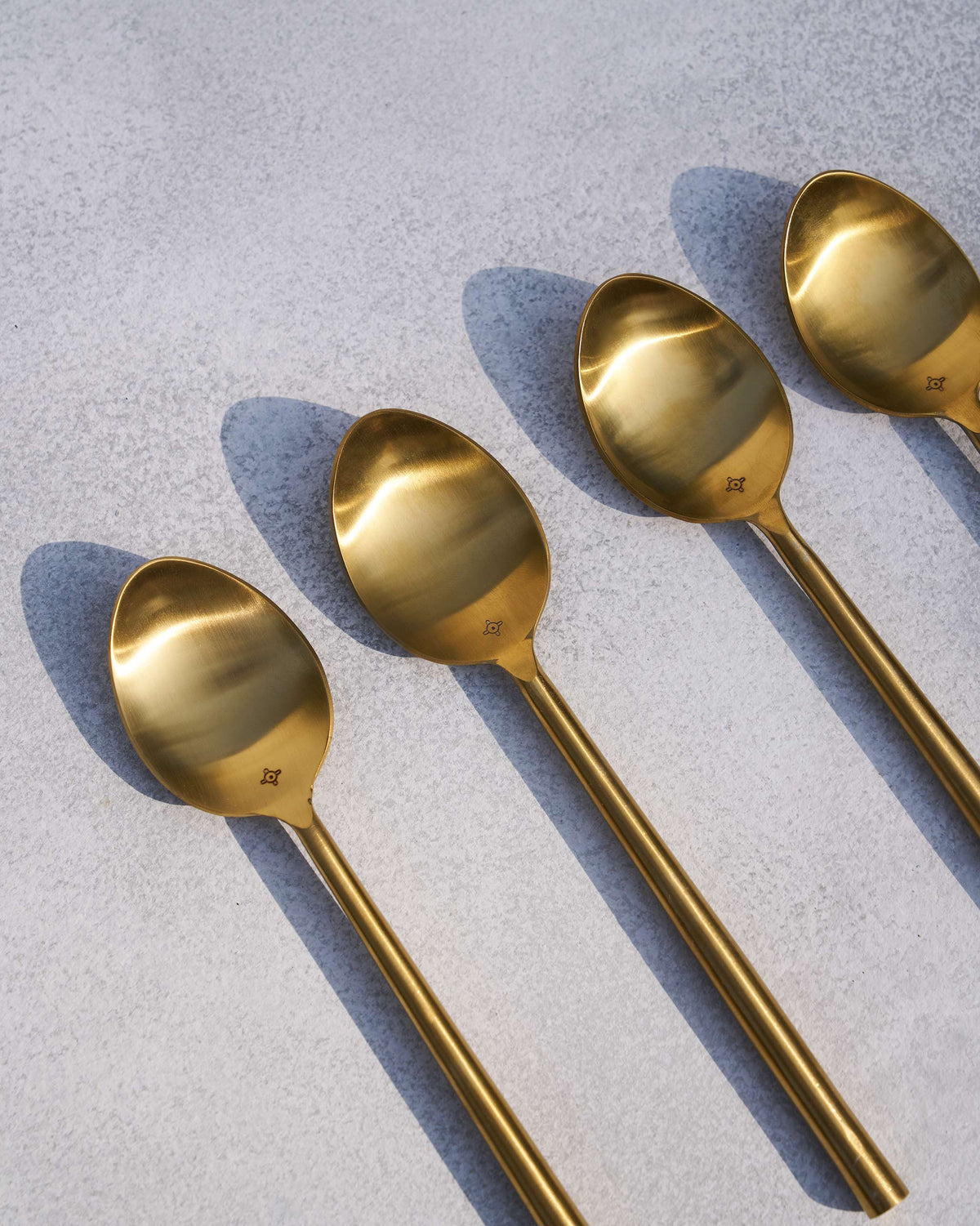 Four brushed gold Sitara spoons laid in a row.