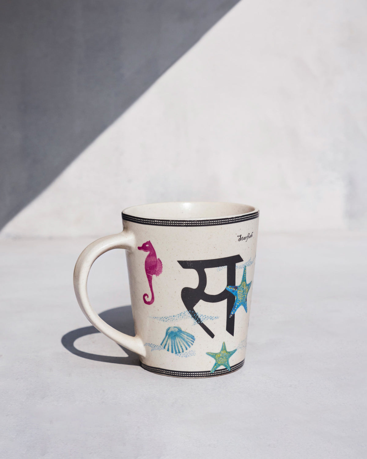 Cream singha mug with a letter S and starfish motif.
