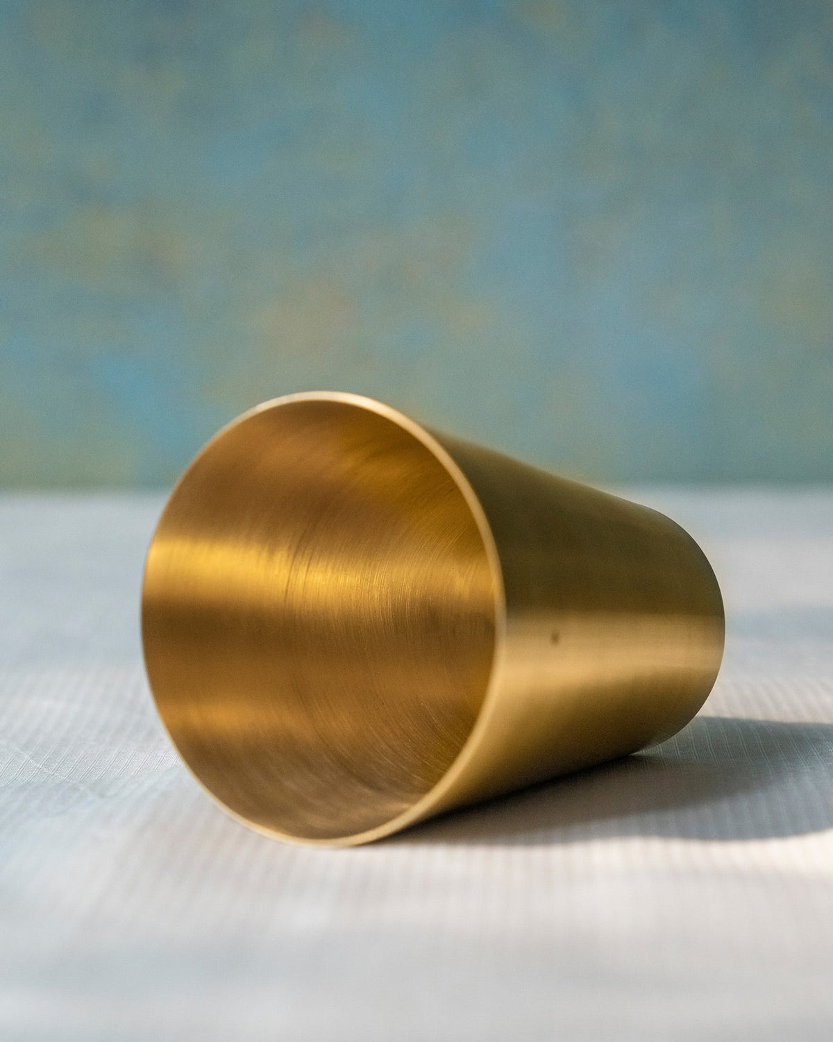Close-up of a brushed brass Madhu glass lying on its side.