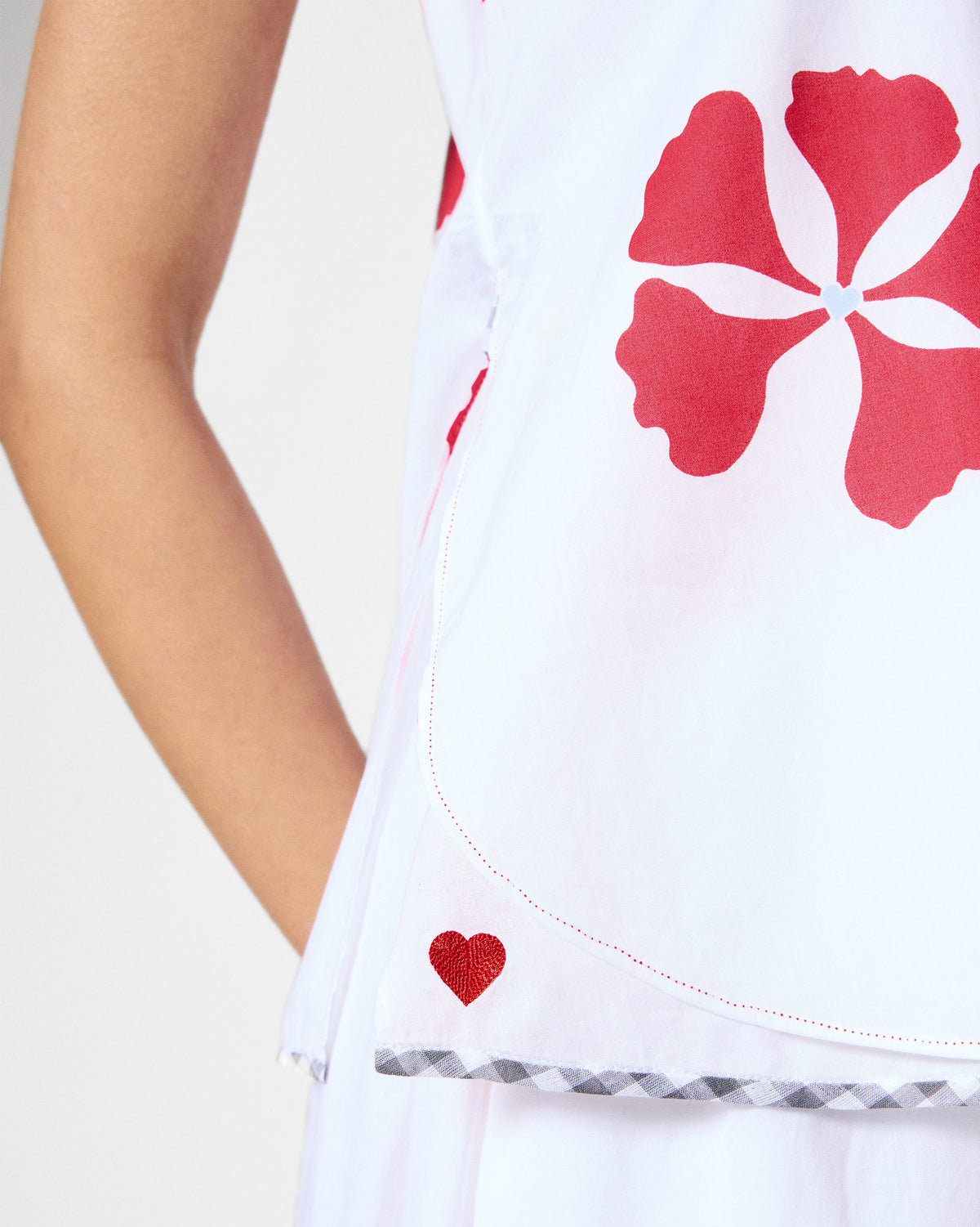 Close-up of the Kiva top's curved hem with a red heart embroidered at the side.