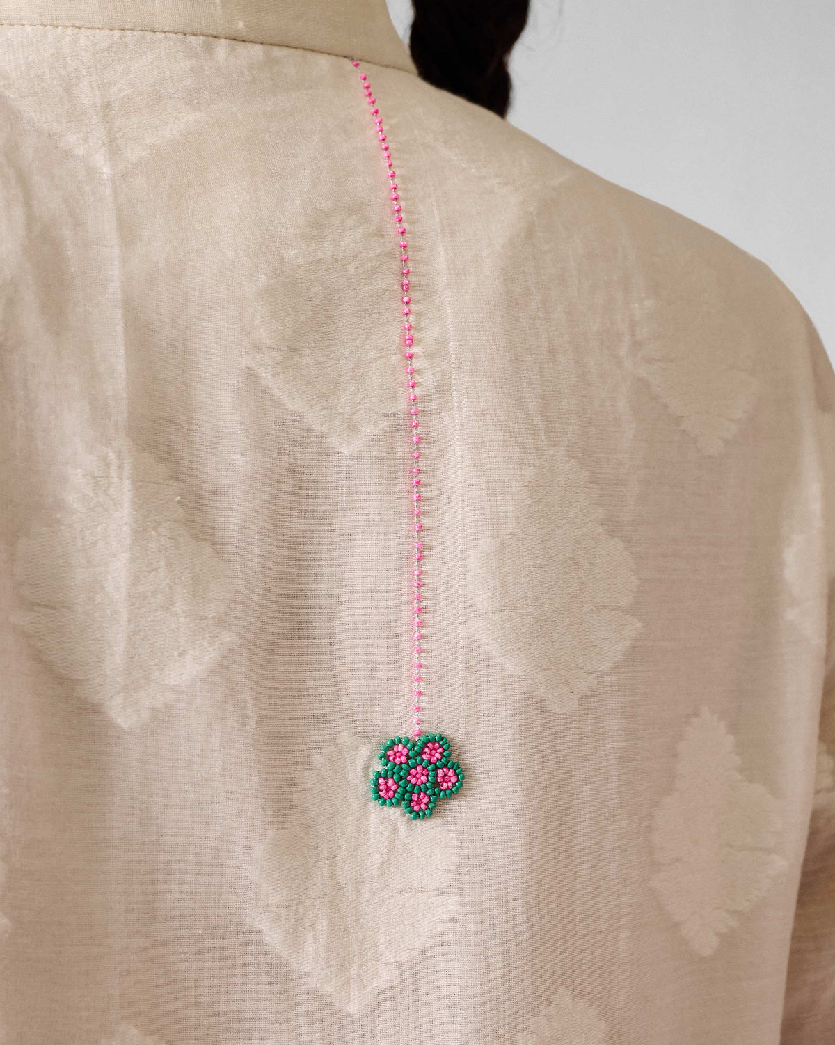 Close-up of a pink and green beaded flower on the back of an ivory kurta.
