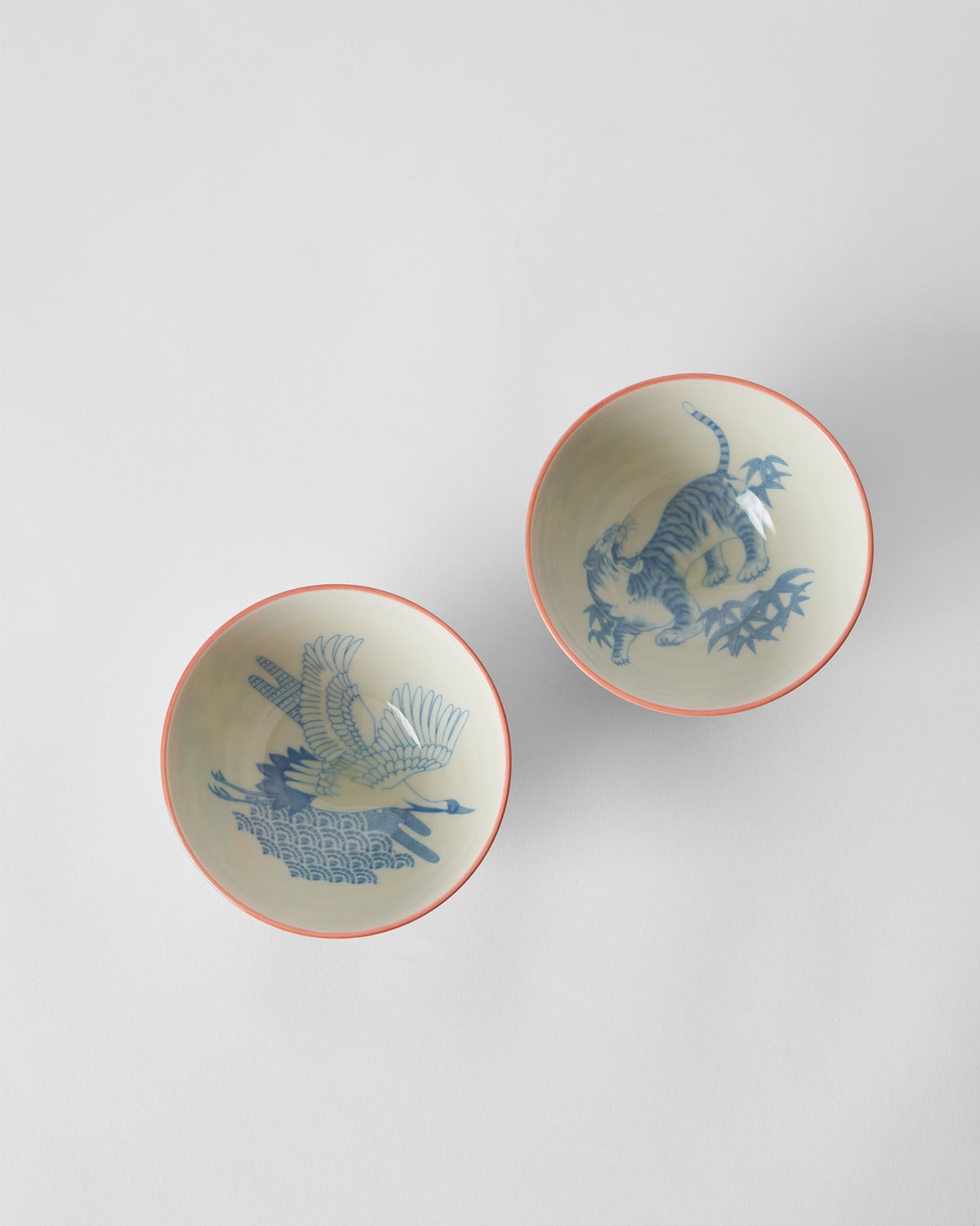 Overhead view of red Crane and Tiger bowls showing blue crane and tiger interiors.