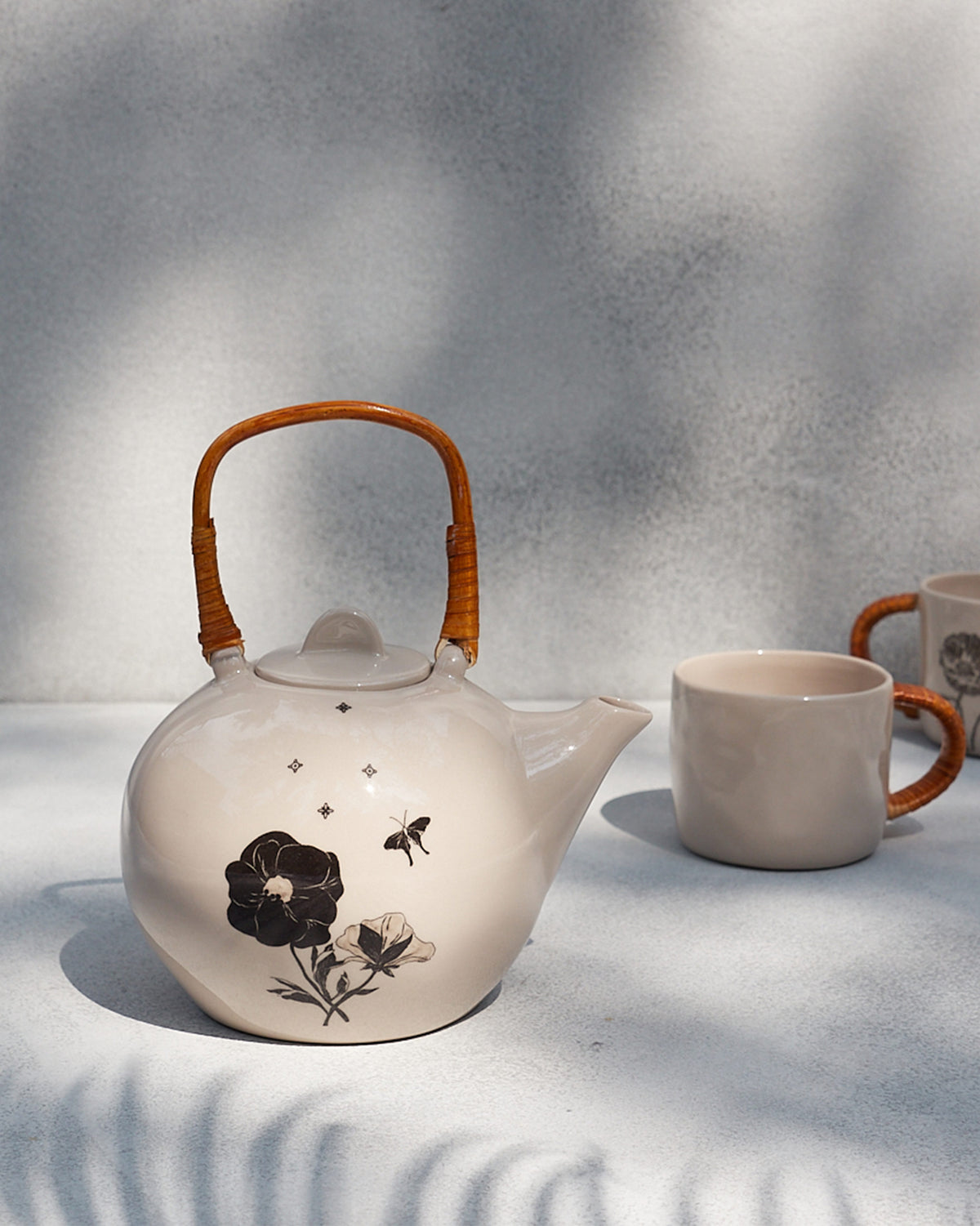 Poppy teapot with rattan handle beside a matching cane-wrapped mug.