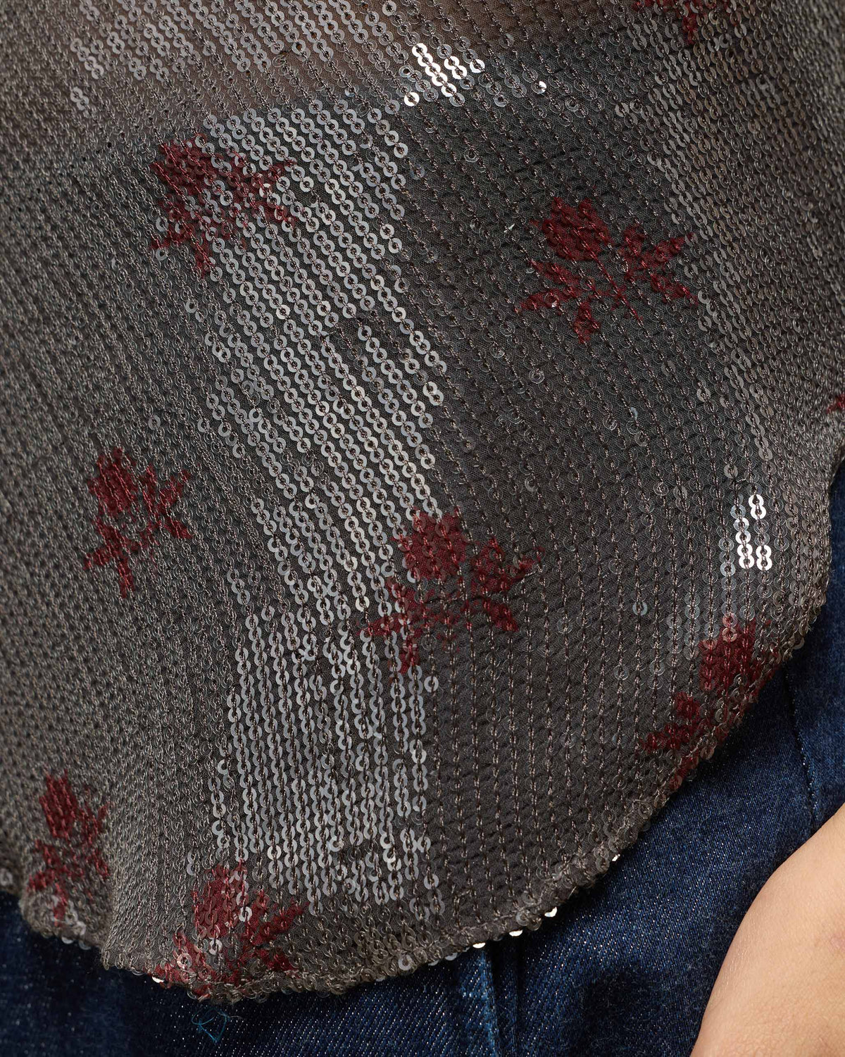 Close-up of sequins and red floral embroidery on a charcoal Flit top.