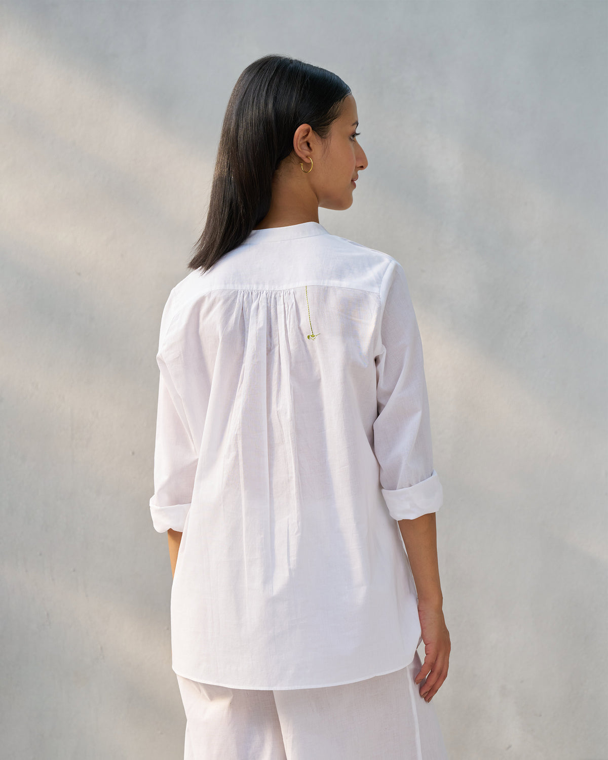Back of a white mandarin collar top with a gathered yoke and green bird.