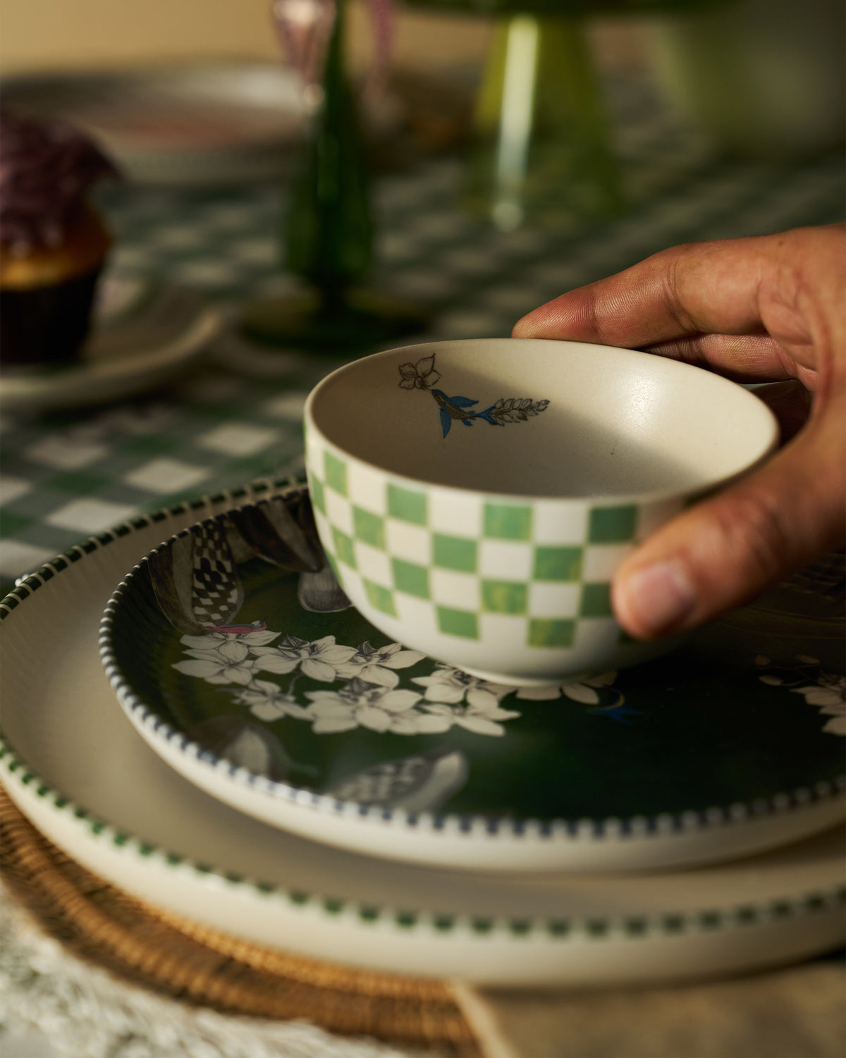 Hand holding a green checked Reesha katori on a floral plate stack.