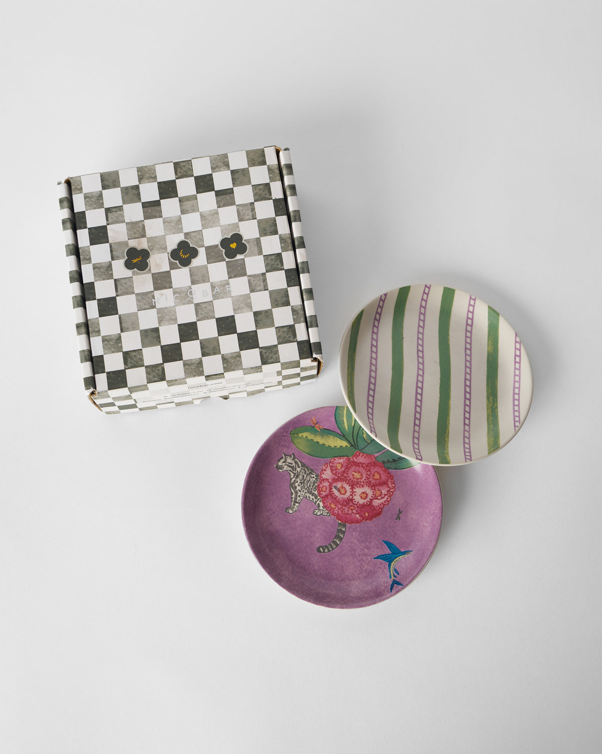Buransh Tea Plates with purple blooms and stripes beside a checkered box.