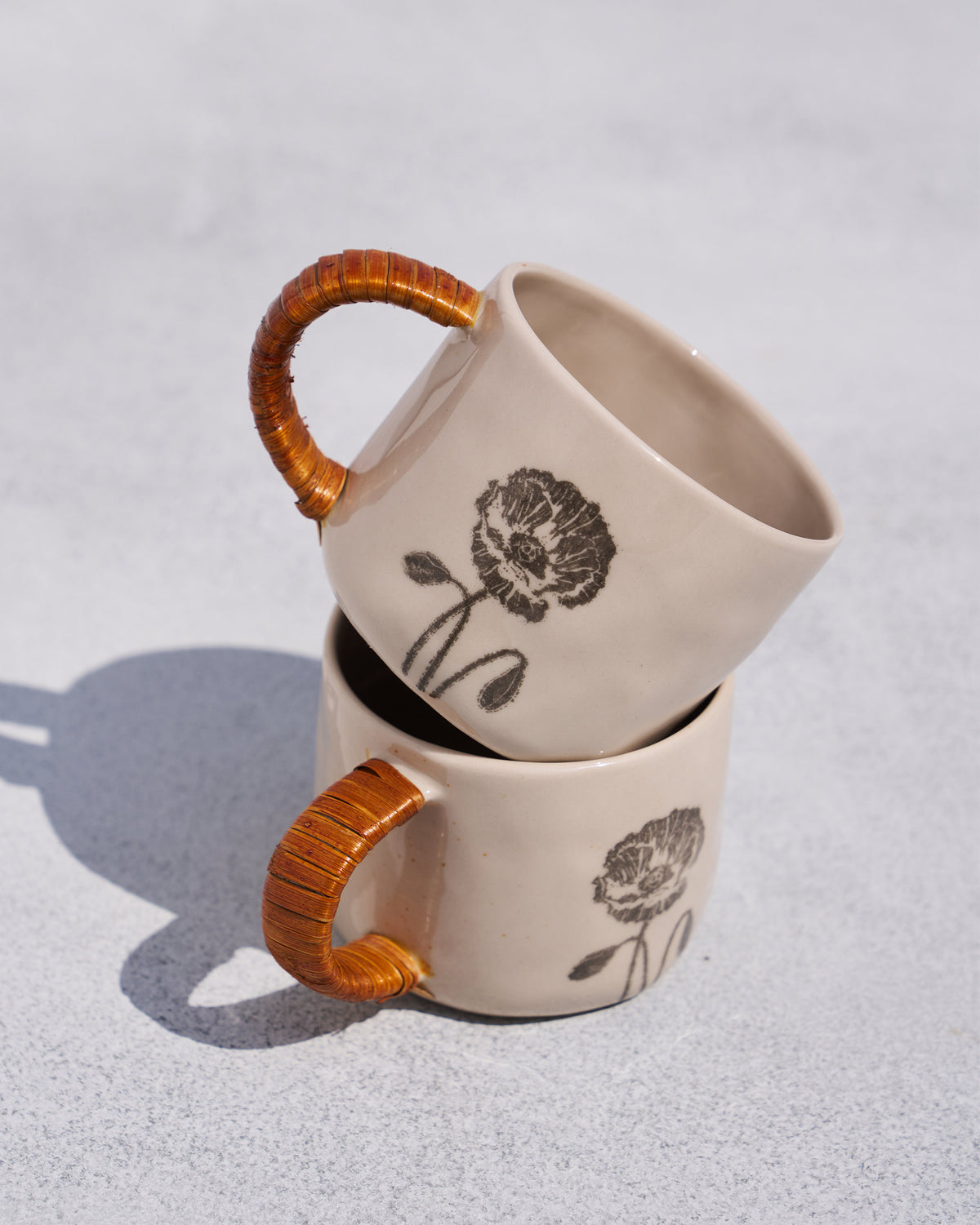 Two Poppy mugs stacked showing rattan handles and poppy prints.