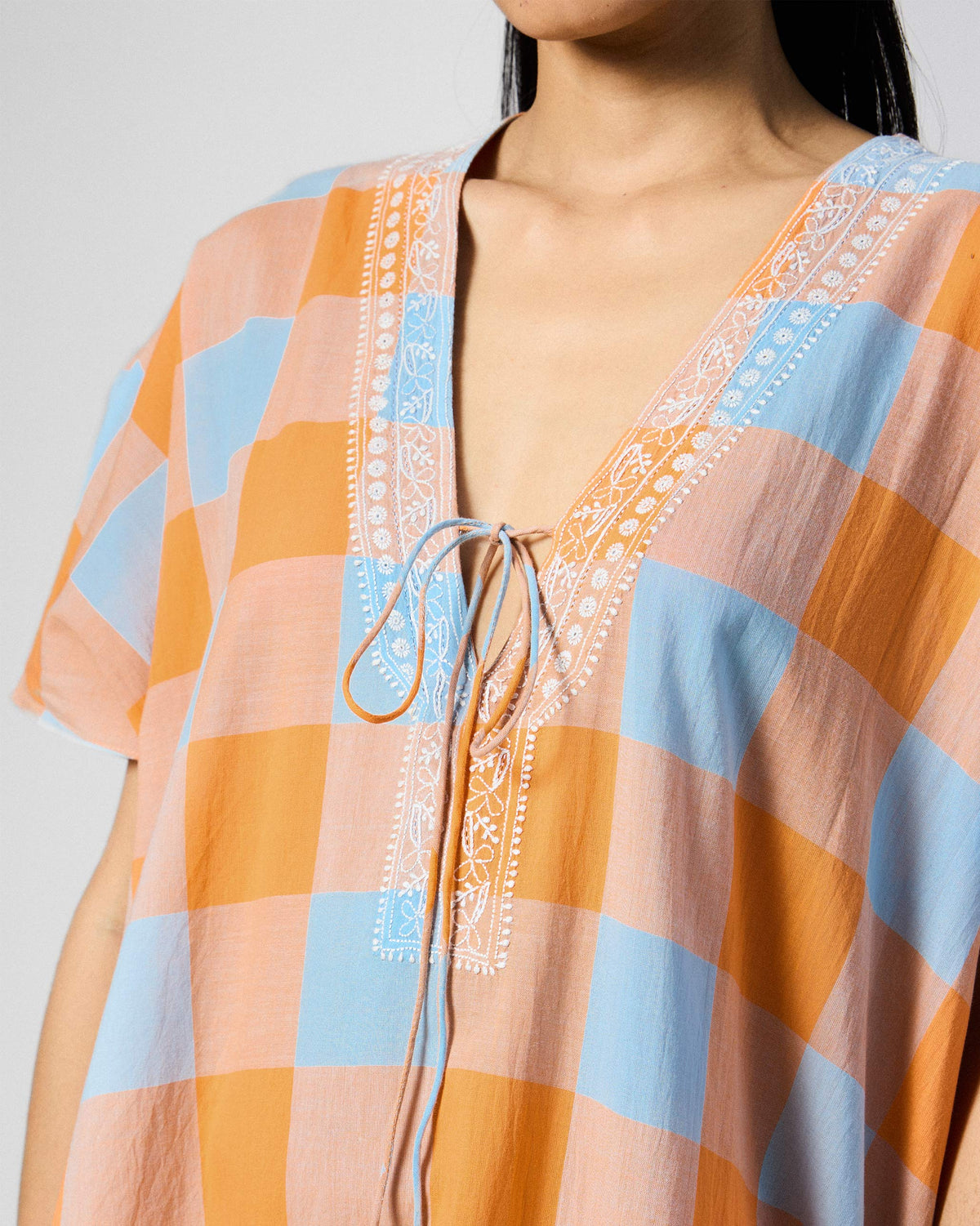 Close-up of white embroidery on the V-neck of an orange check Vaya kaftan.