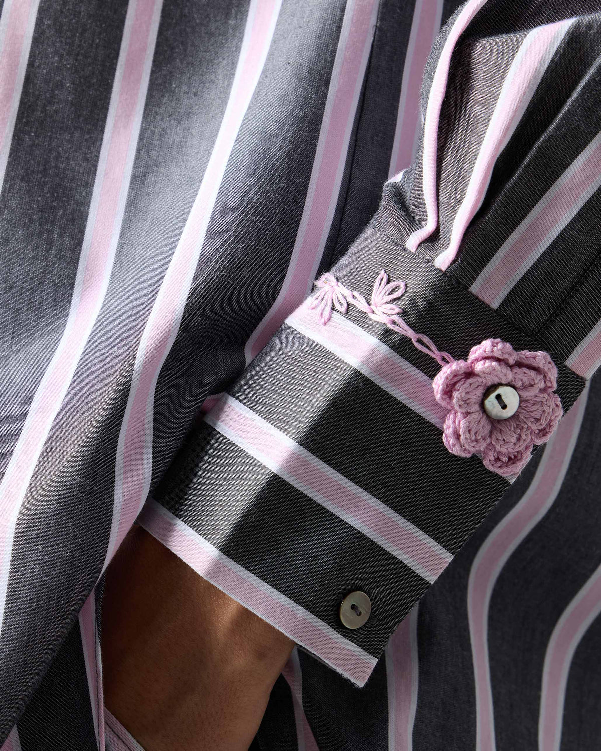 Close-up of a Trench shirt cuff with a pink crochet flower.