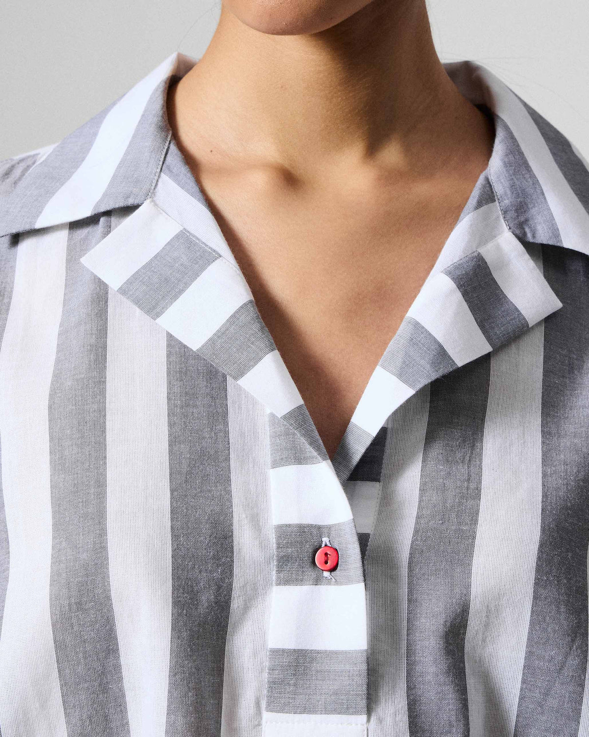 Close-up of a grey and white striped Rann shirt with a red neckline button.