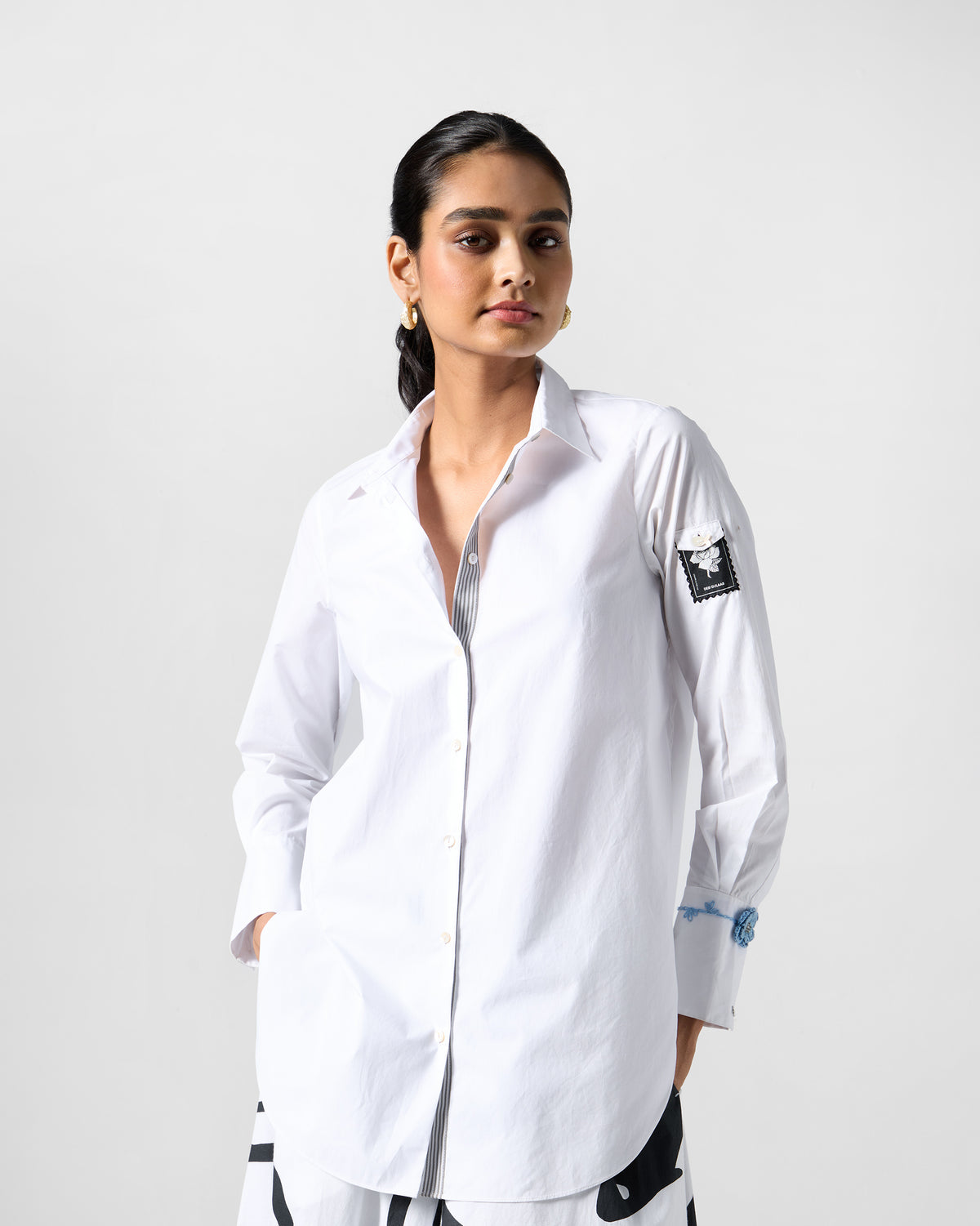 Person wearing a white trench shirt with a sleeve stamp and blue crochet cuff.