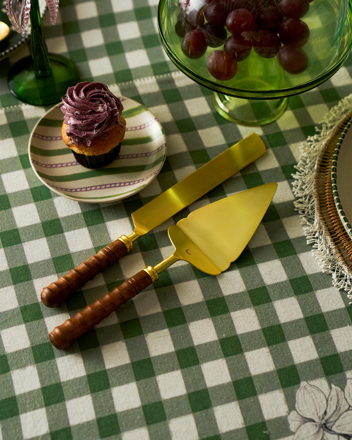 Gold cake knife and server set on a green checkered tablecloth.