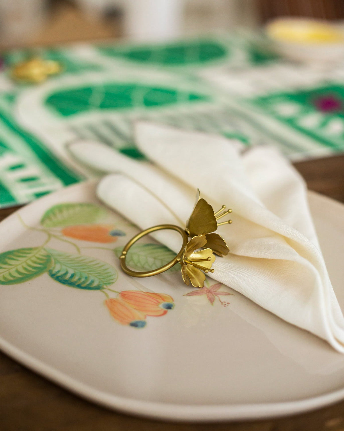 Close-up of a gold floral napkin ring from the Jungle Table Set on a plate.