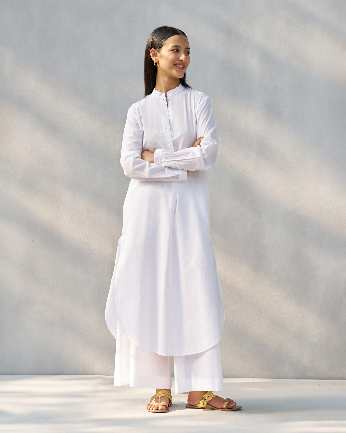 Person wearing a white long kurta set with a curved hem and wide pants.
