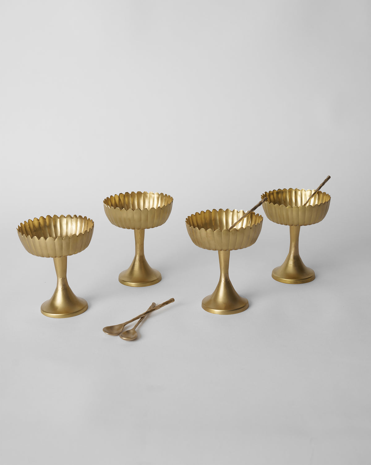 Four gold Dhaara Gelato Cups lined up with matching brass spoons.