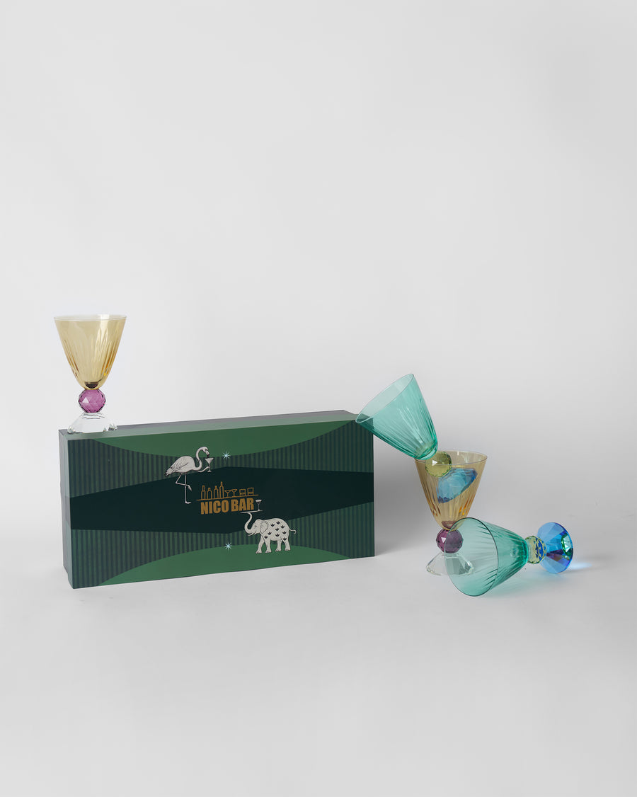 Four Vira cocktail glasses in teal and amber beside their green Nico Bar gift box