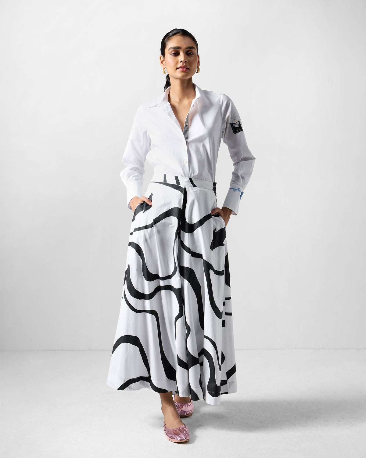 Person wearing a white trench shirt set with black wave-print flared pants.