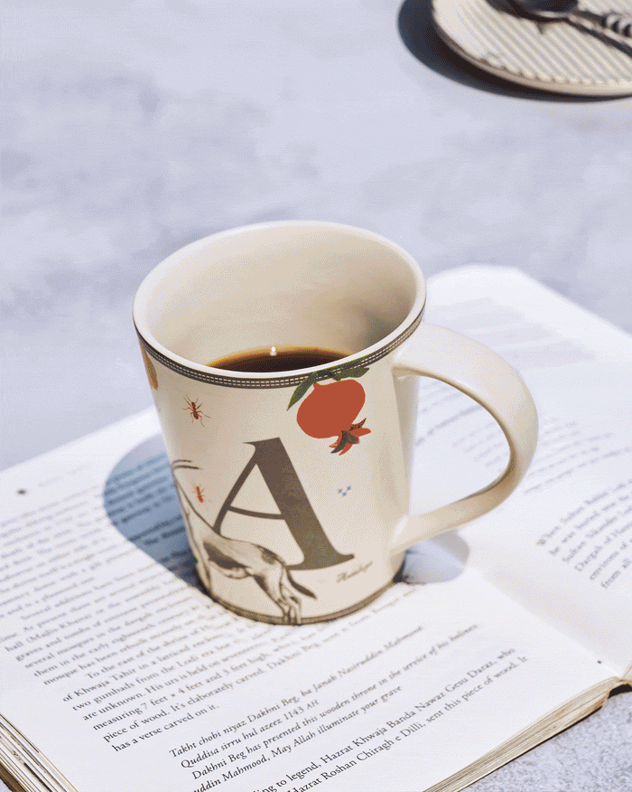 Cream Ananas alphabet mug with a letter and fruit motif, filled with coffee.