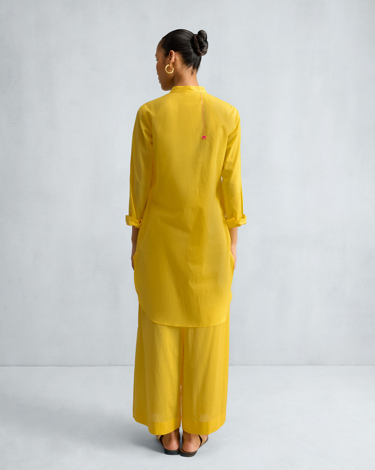 Back of a yellow mid-length kurta set with a curved hem and matching trousers.