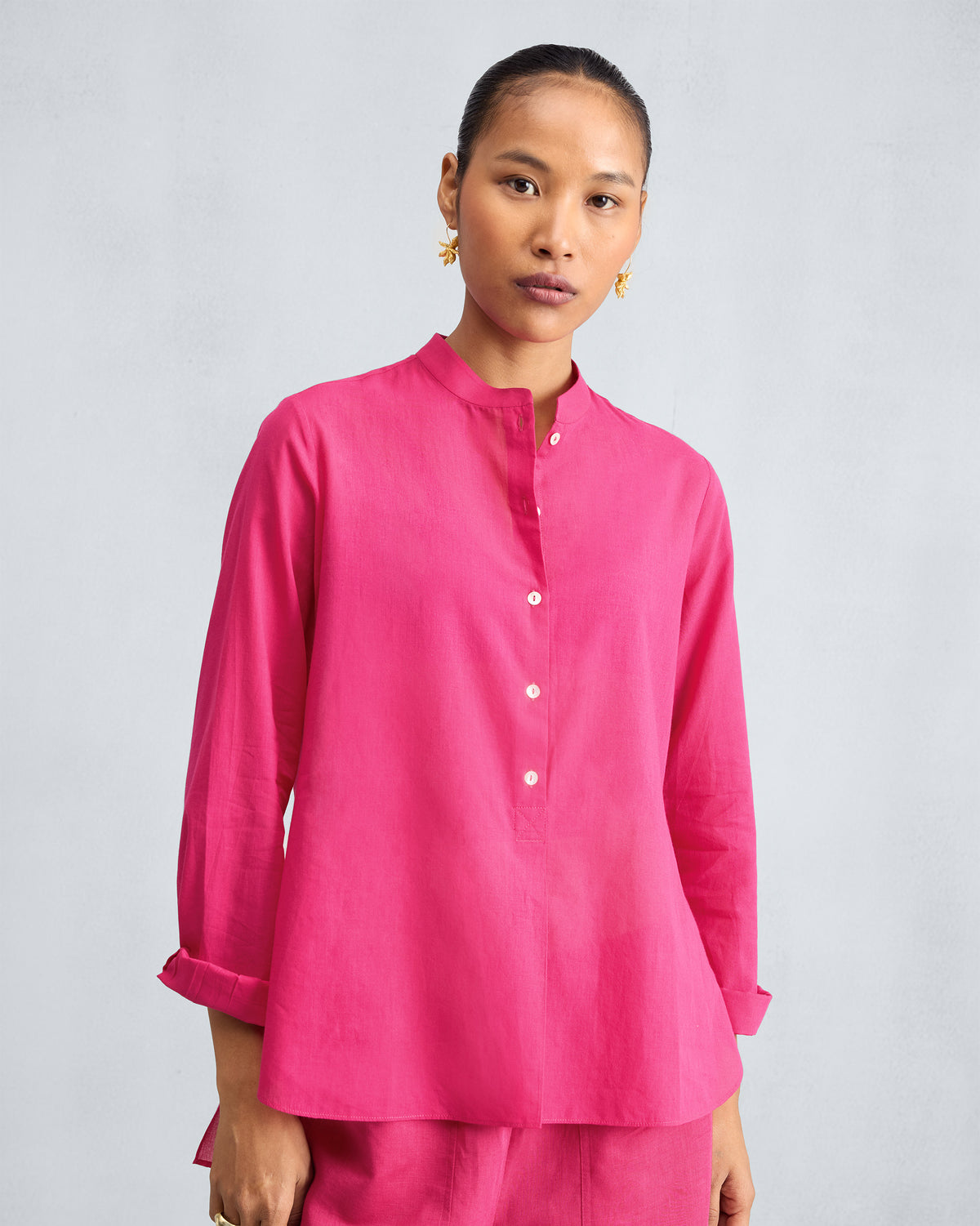 Person wearing a fuchsia mandarin collar top with a button placket.