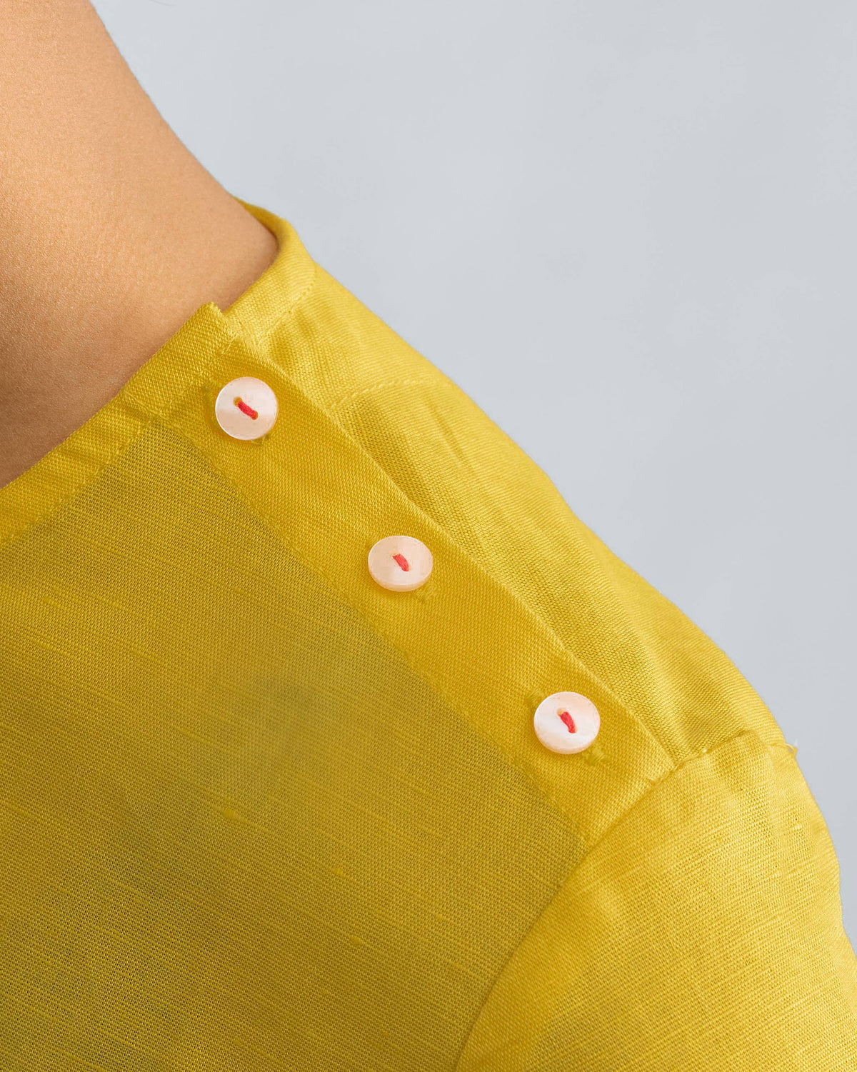 Close-up of shoulder buttons with red stitching on a yellow high slit top.