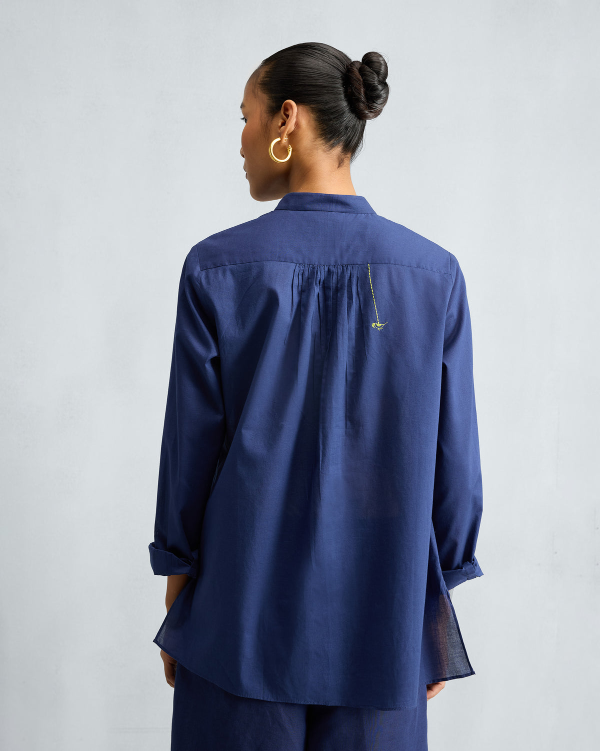 Back of an ink blue top with a yoke and small yellow embroidery.