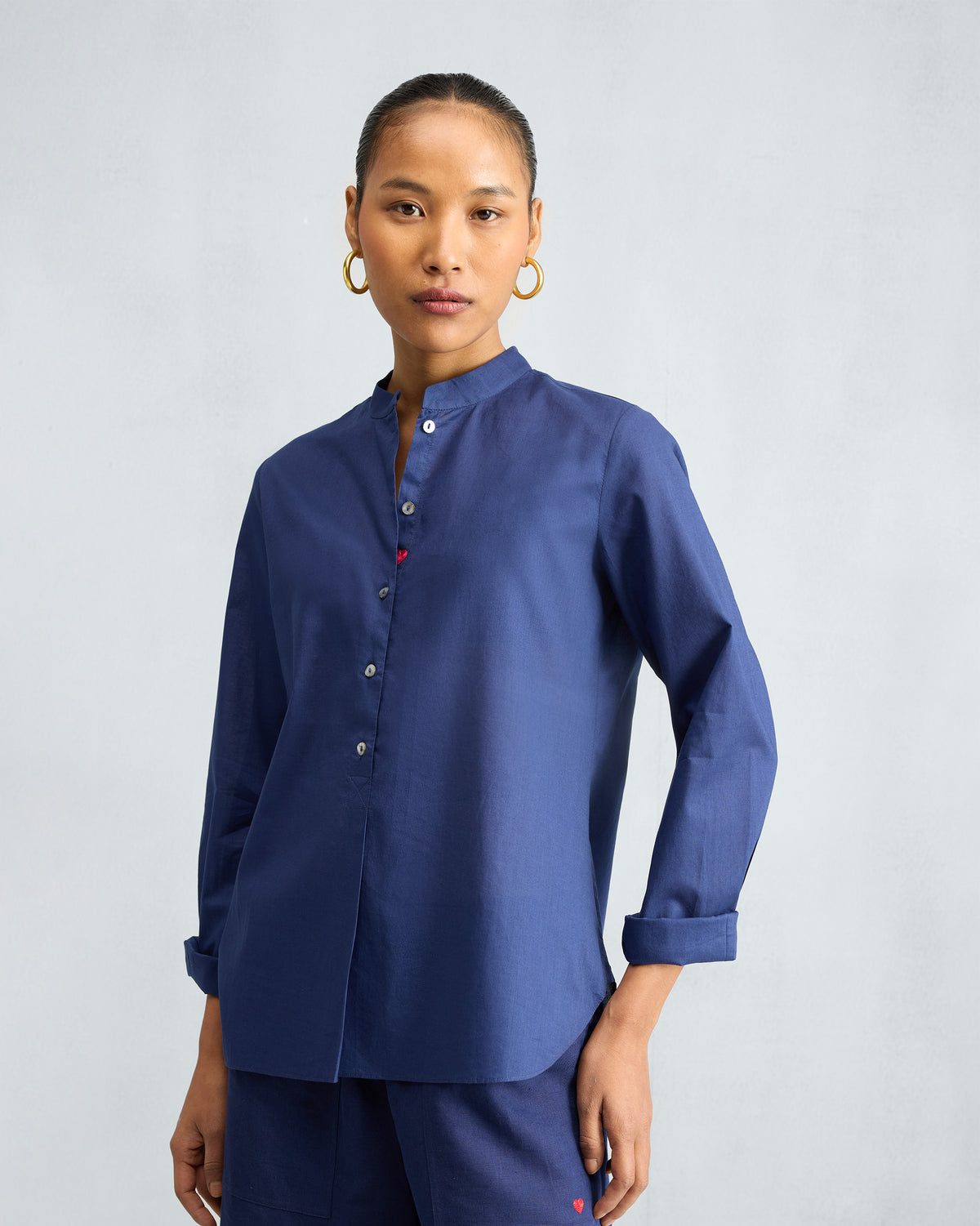 Person wearing an ink blue mandarin collar top with a small red heart at the hem.