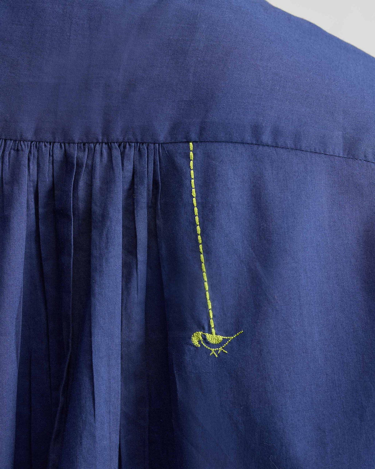 Close-up of neon green bird embroidery on the back of an ink blue top.