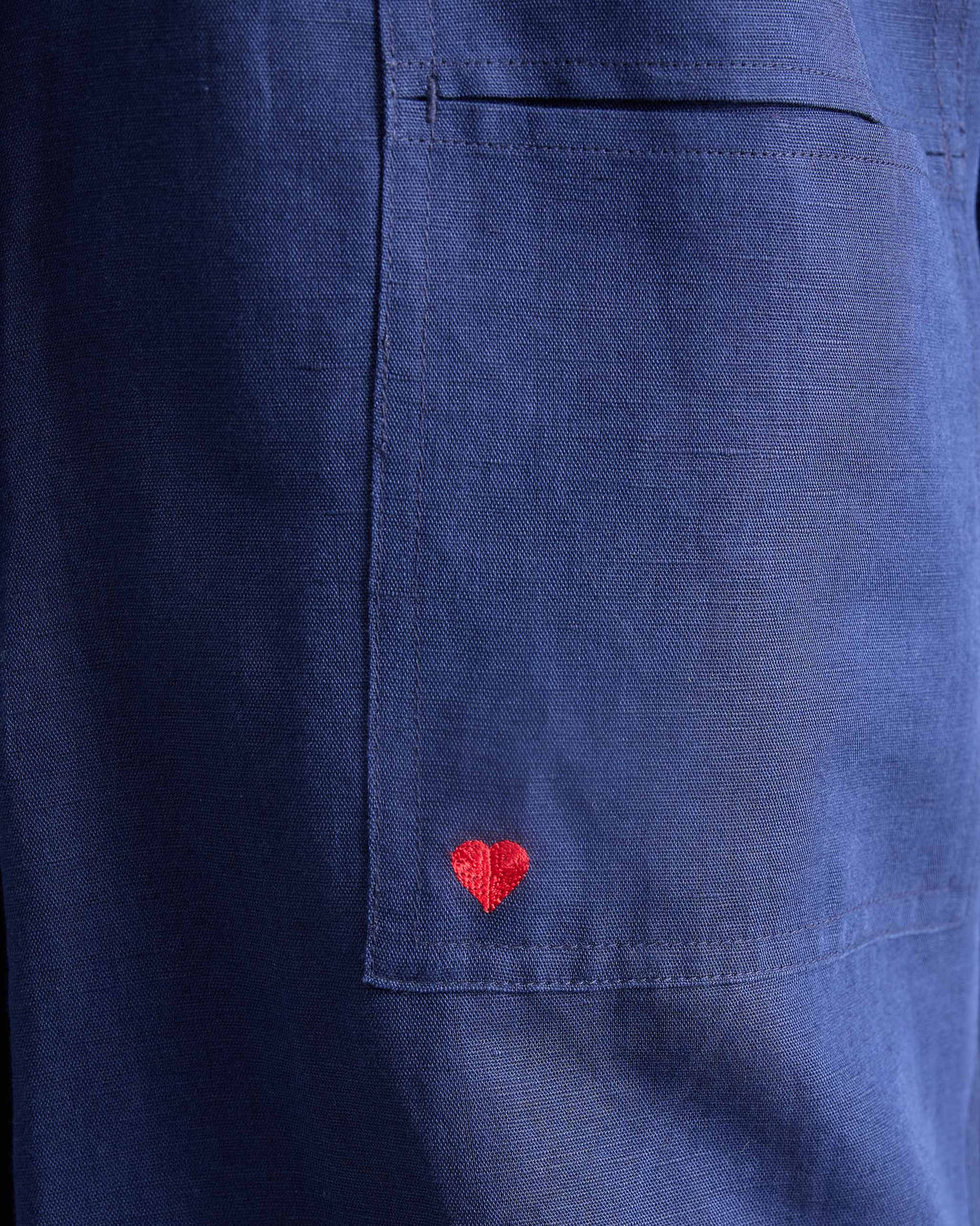 Close-up of a red heart embroidery on the pocket of ink blue pants.