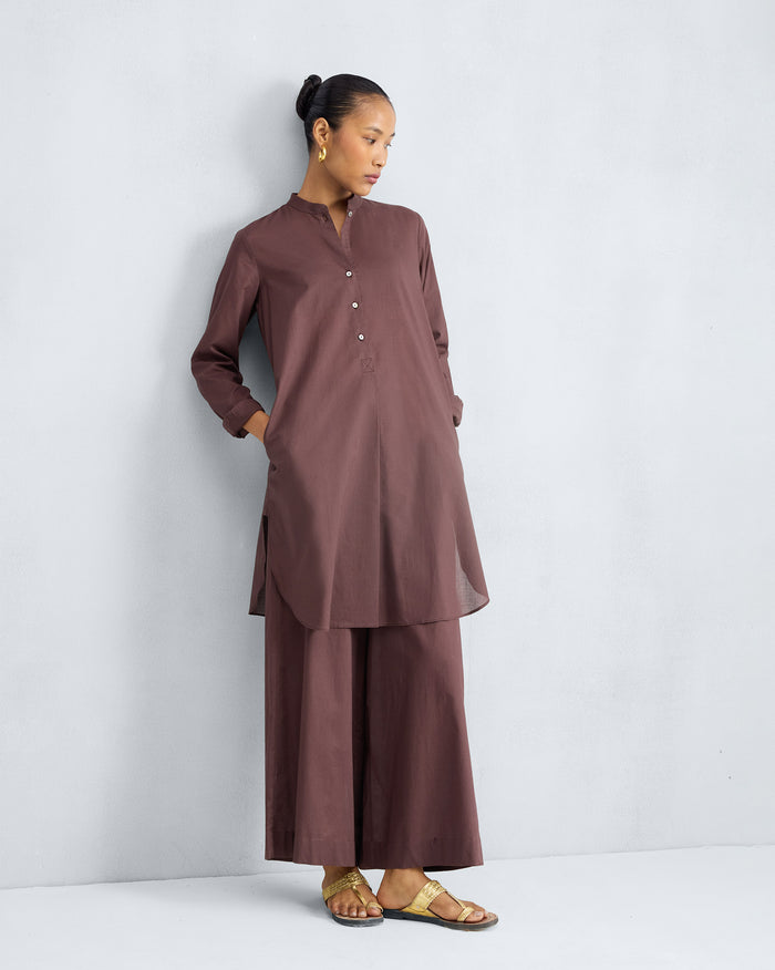 Person wearing a chocolate plum mid-length kurta set with hands in the pockets.