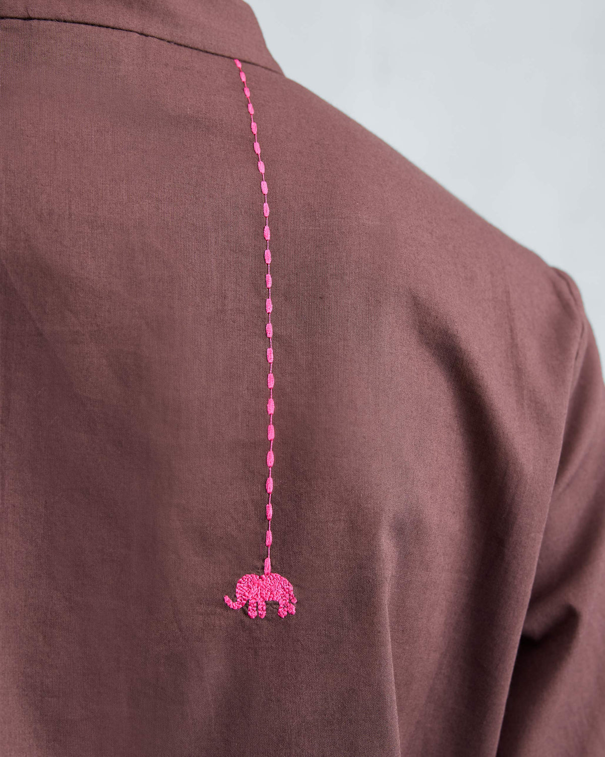 Close-up of a pink elephant embroidery on the back of a chocolate plum kurta.