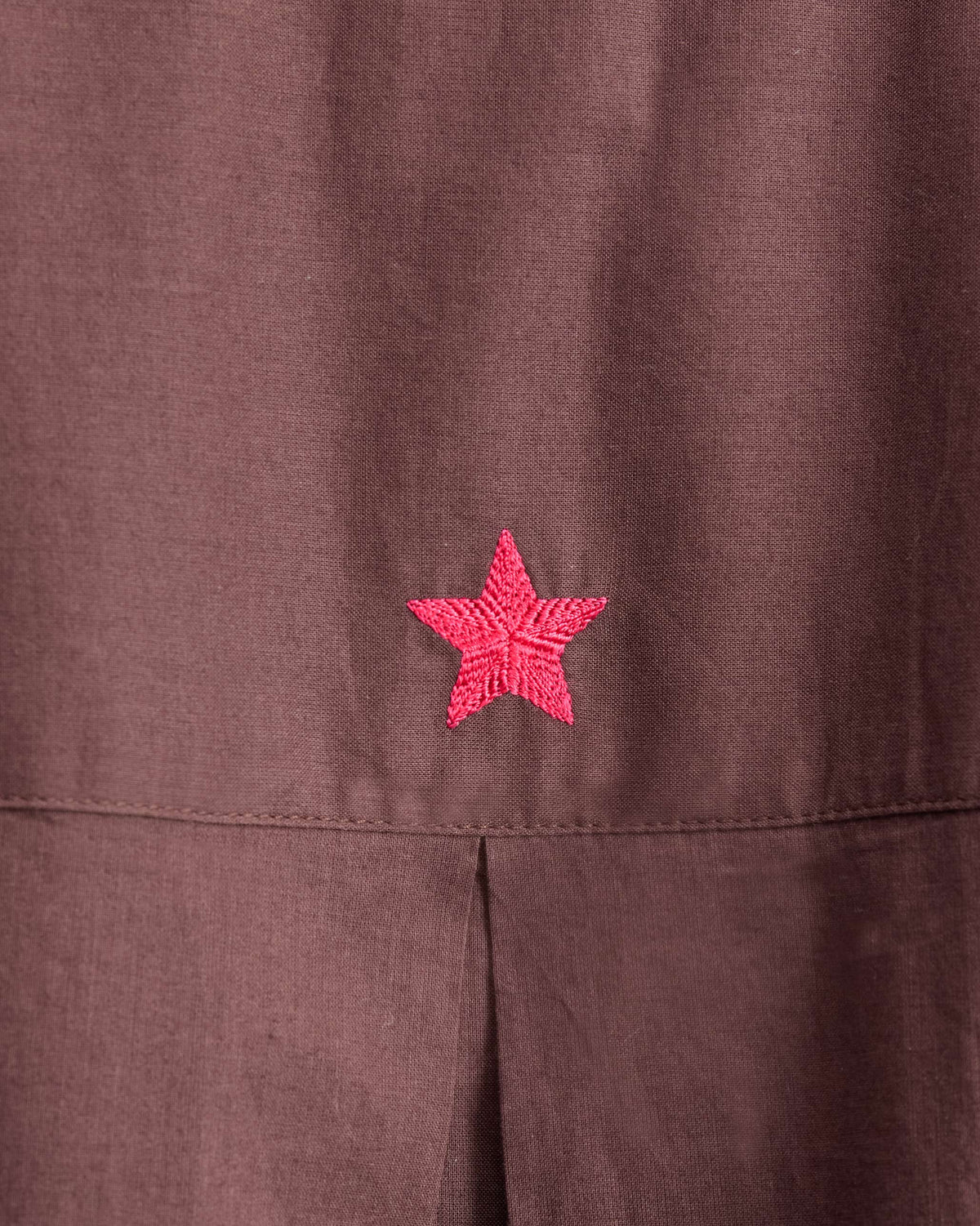 Close-up of a pink embroidered star on a chocolate plum tunic yoke.